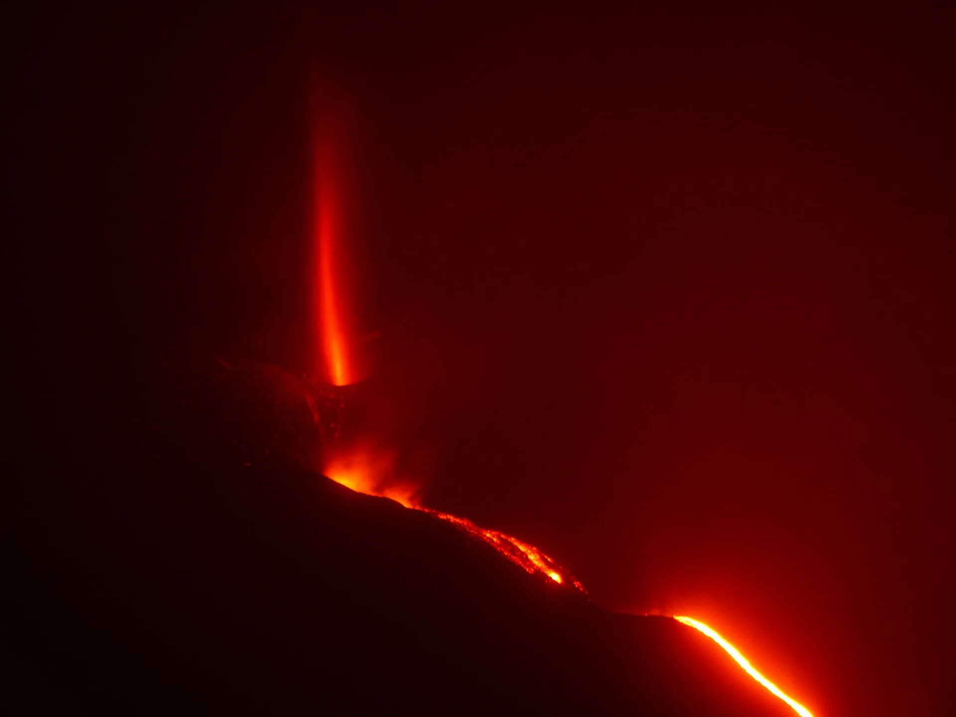 Der Vulkanausbruch auf La Palma im November 2021 bei Nacht: eine Lavafontäne und ein glühender Lavastrom