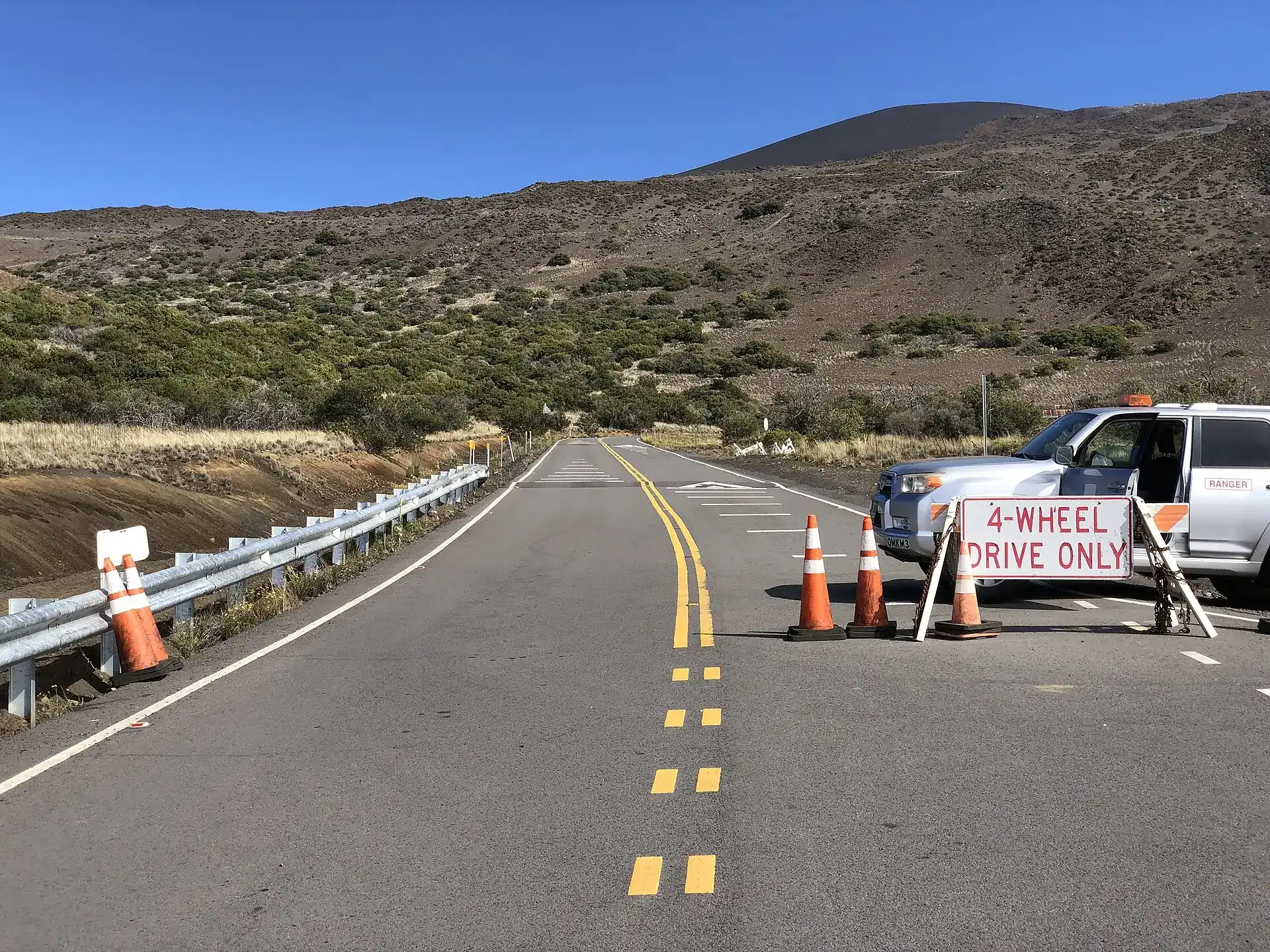 Start of the summit road at the Mauna Kea Visitor Information Station: a “4-Wheel Drive Only” sign, traffic cones and a ranger vehicle