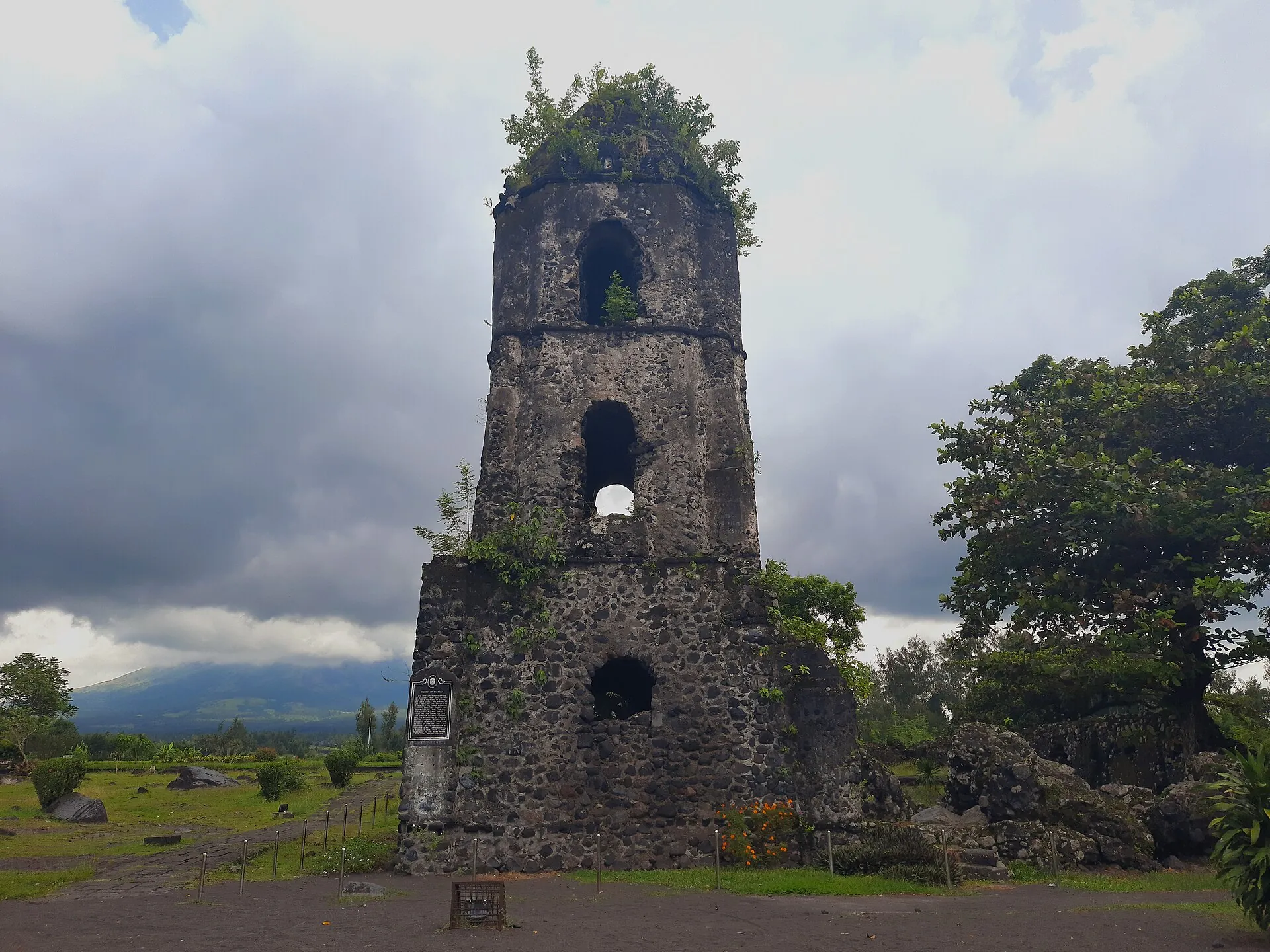 Der Glockenturm der Ruine von Cagsawa steht zwischen Palmen, dahinter erhebt sich der Kegel des Mayon