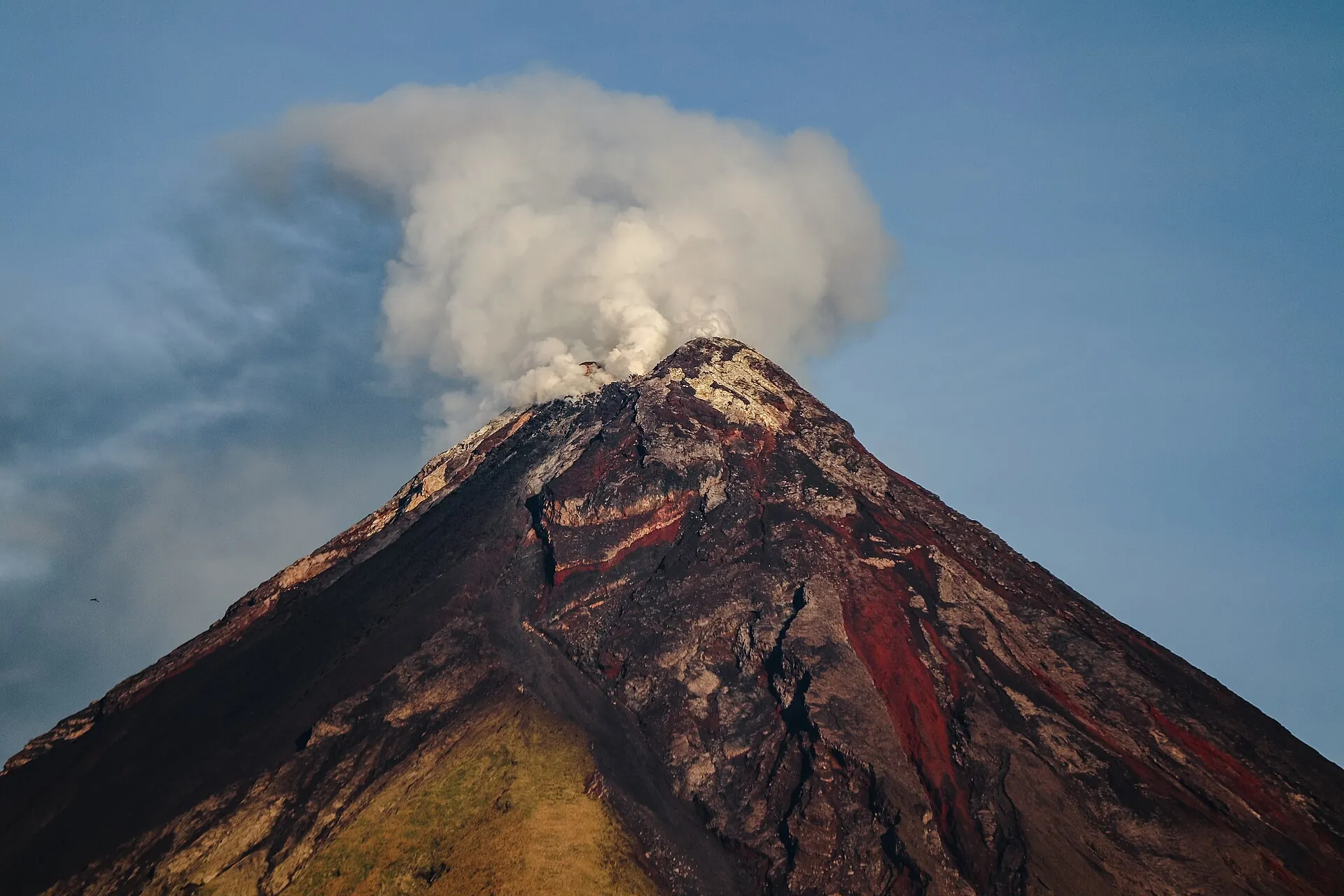 Der Gipfel des Mayon aus der Nähe: eine Dampffahne zieht über den Kraterrand, die Flanken von Rinnen durchzogen