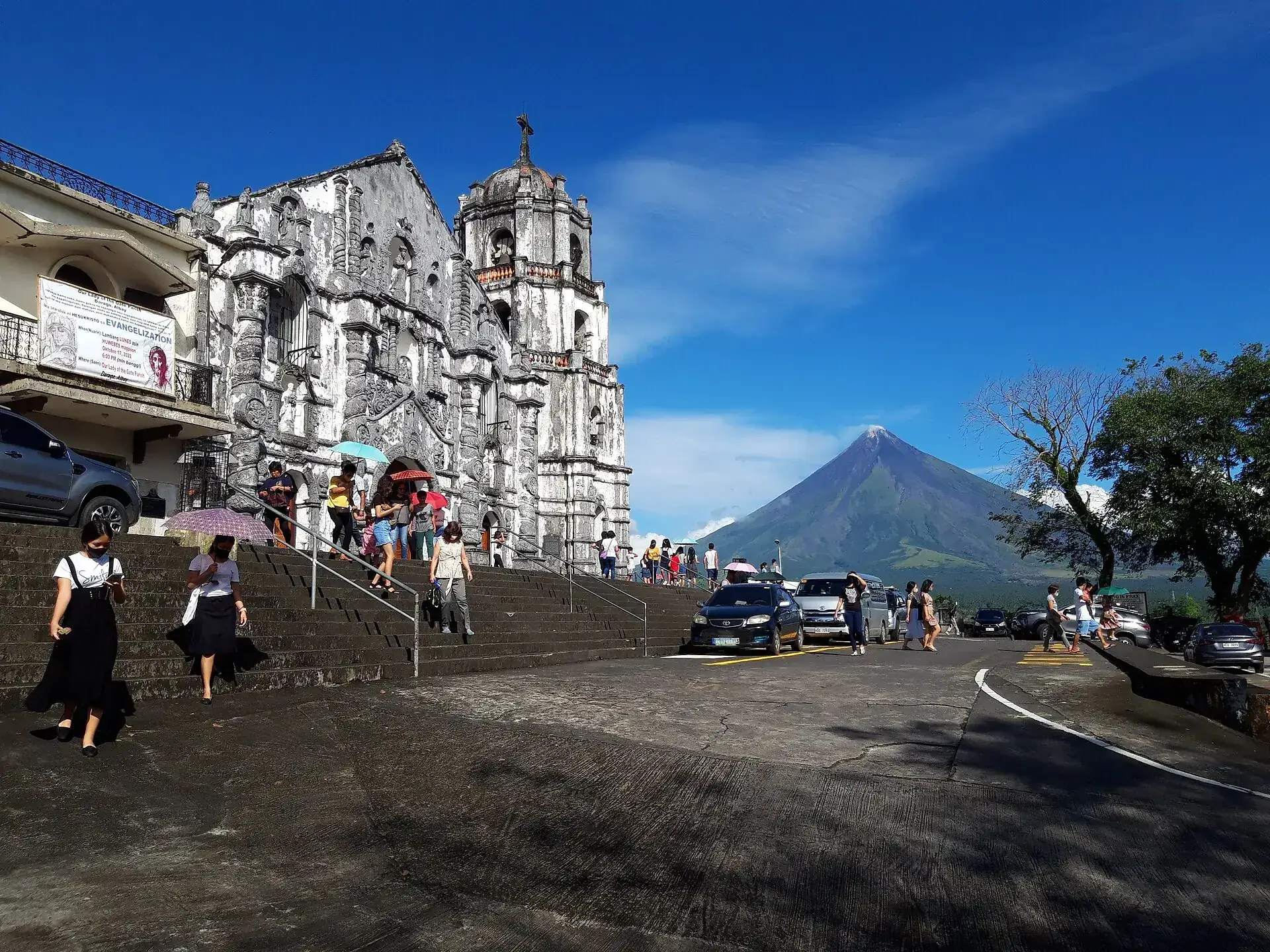 Die weiße Barockkirche von Daraga auf ihrem Hügel, dahinter der Kegel des Mayon unter blauem Himmel