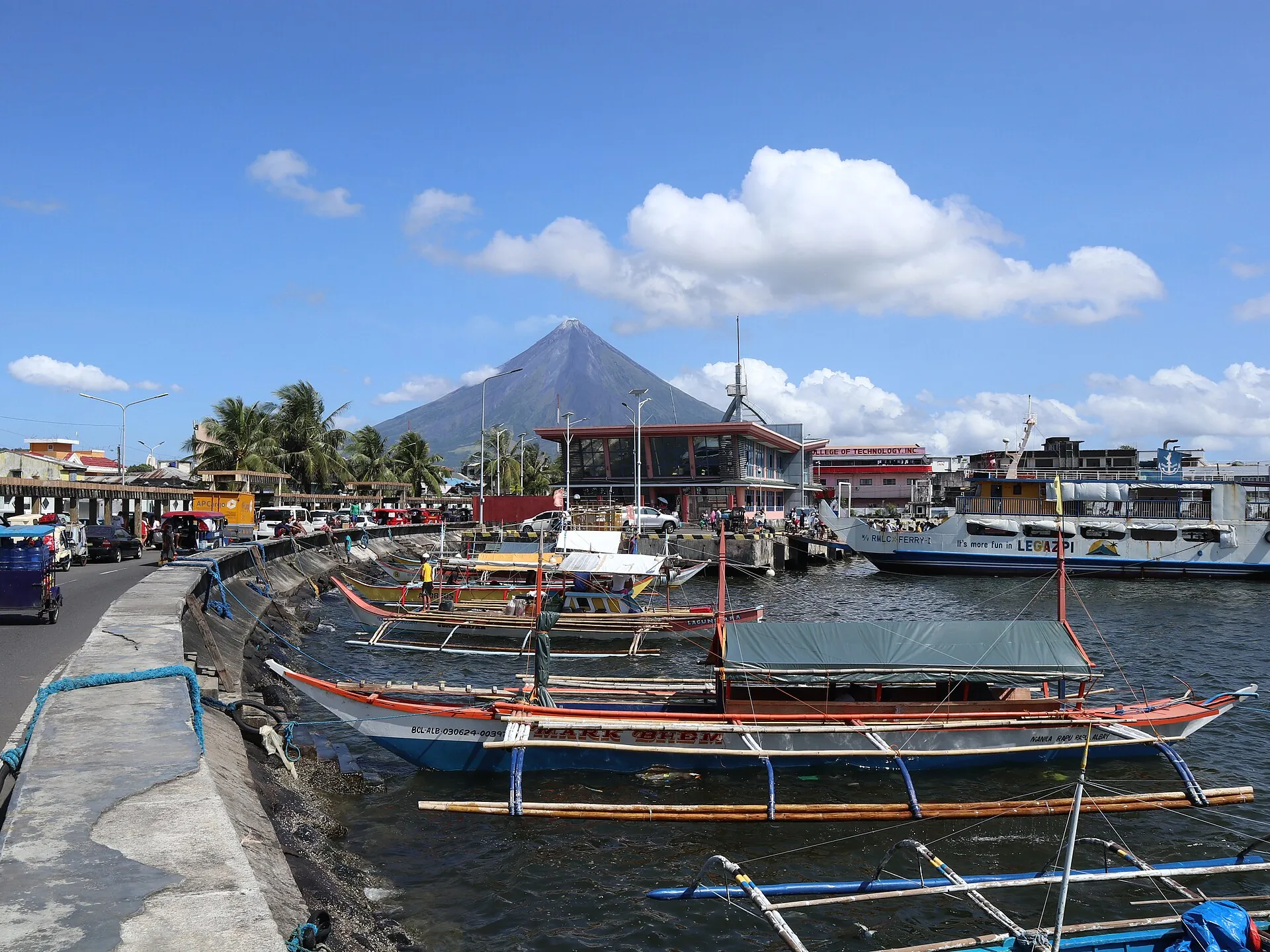 Der Mayon über dem Hafen von Legazpi, im Vordergrund Fischerboote und Kaimauer, der Gipfel in dünnen Wolken