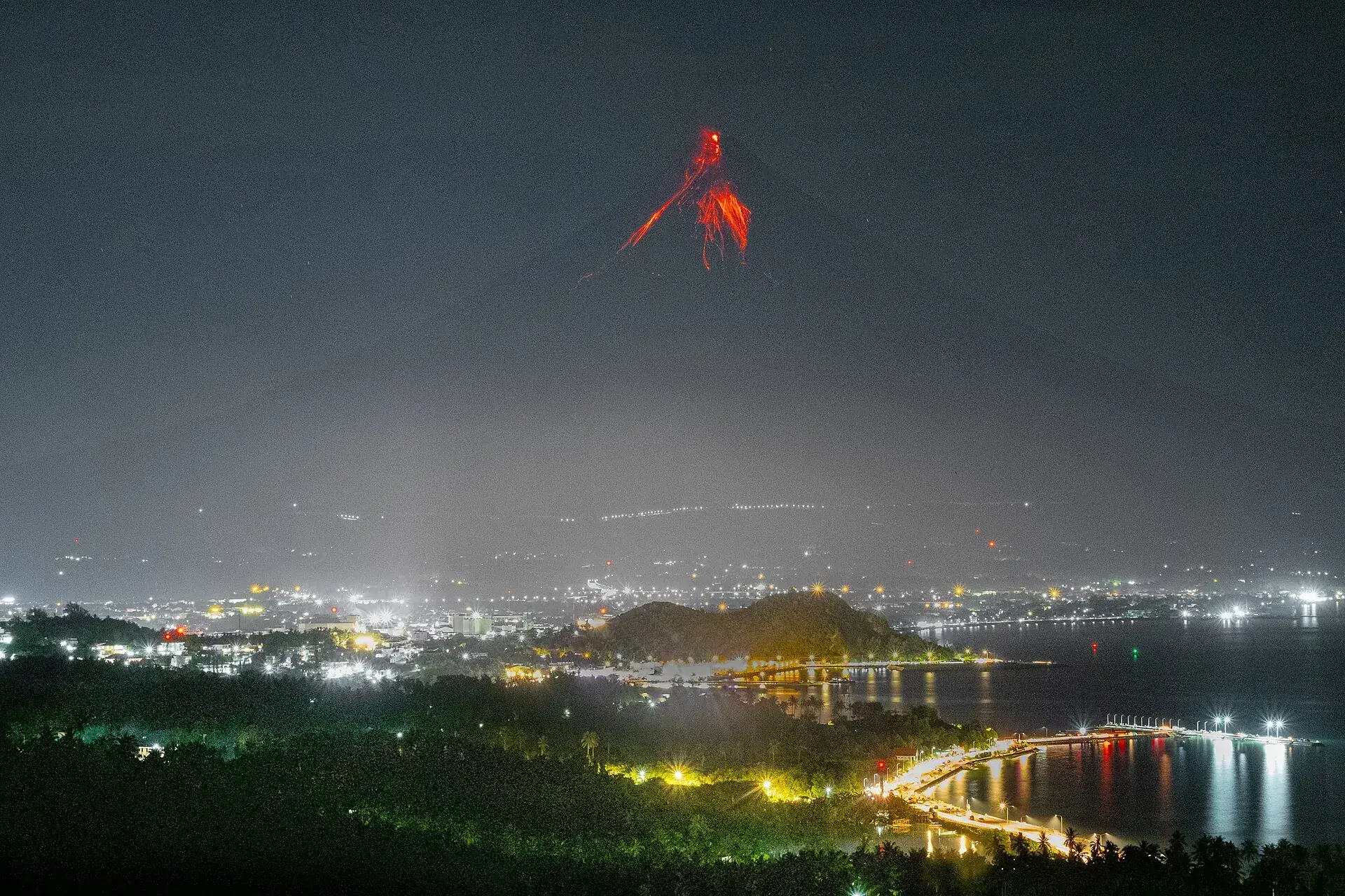 Der Mayon bei Nacht während eines Ausbruchs: glühende Lava läuft in Bändern vom Gipfel die Flanke hinunter