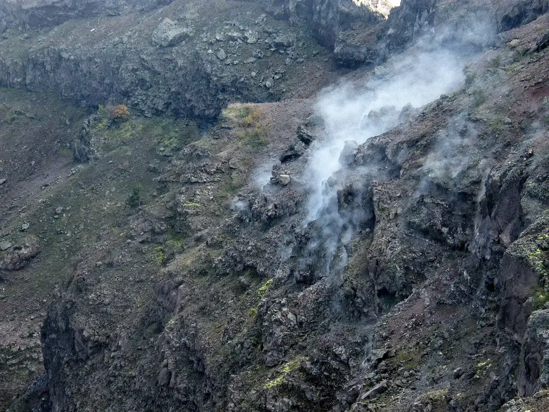 A fumarole on the crater rim of Mount Vesuvius, steam rising from reddish rock