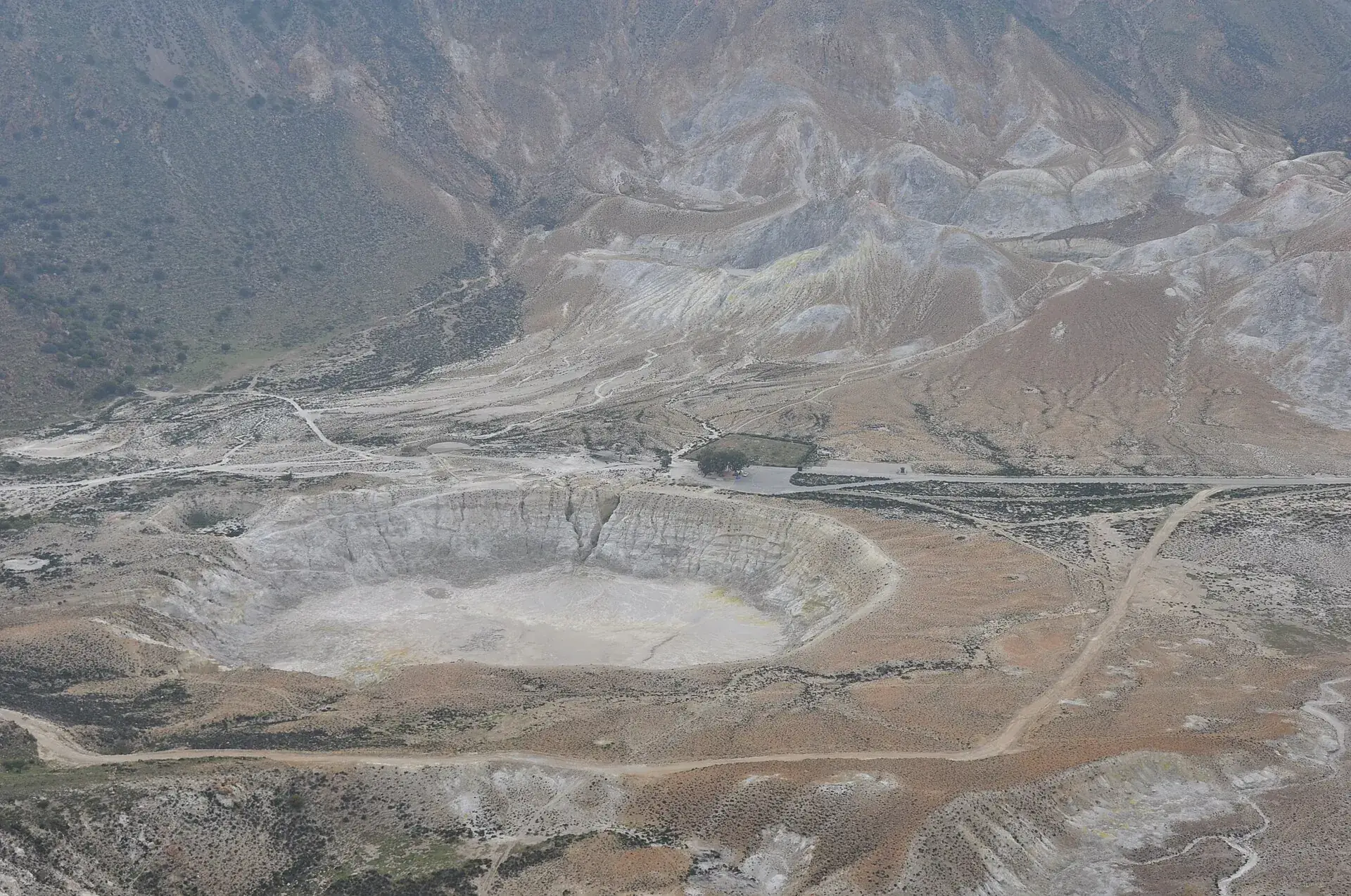 Der Stefanos-Krater auf Nisyros von oben: der helle Kraterboden, daneben Parkplatz und Zufahrtsstraße durch die Caldera