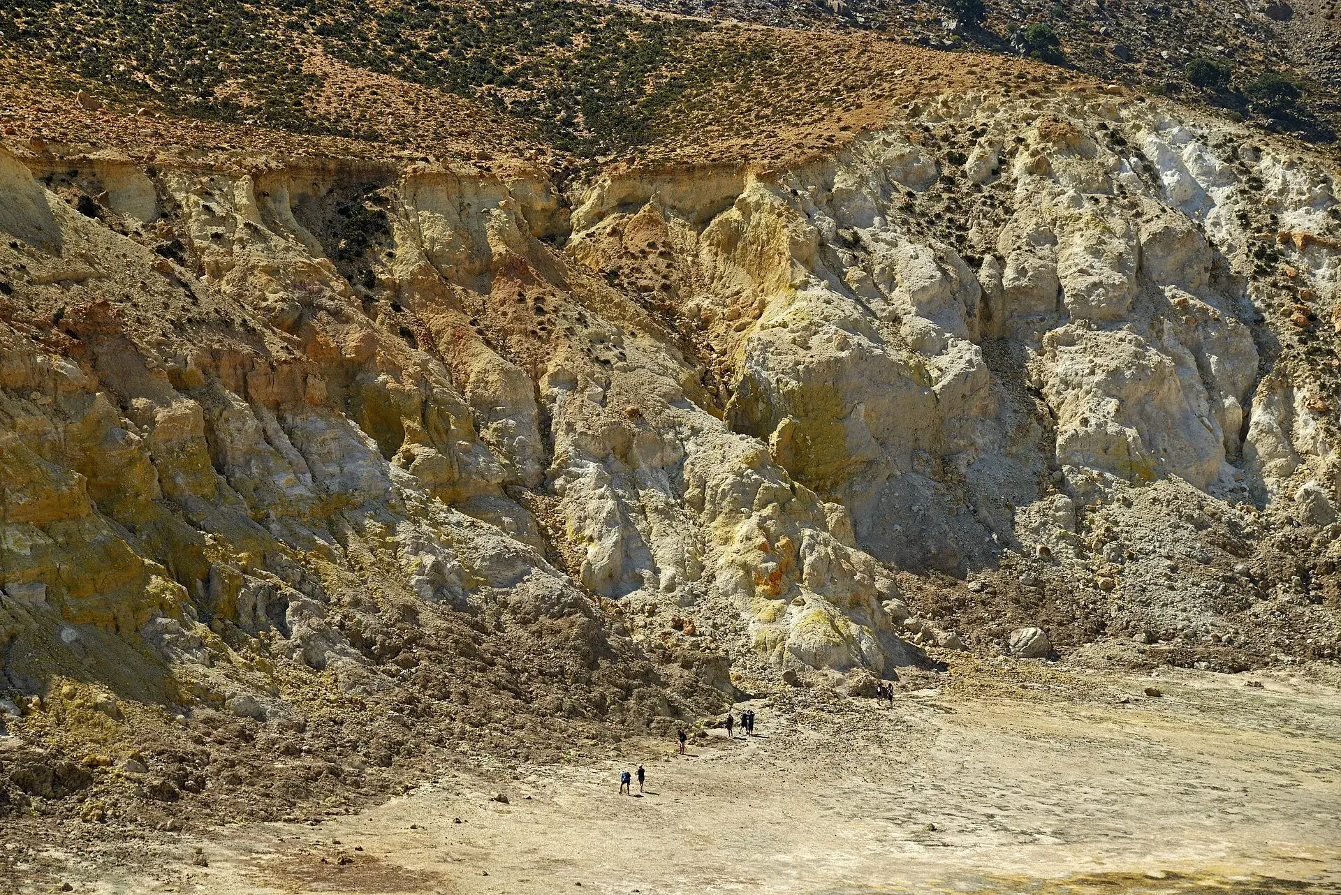 Die Südwand des Stefanos-Kraters auf Nisyros mit gelben Schwefelablagerungen, winzige Menschen auf dem Kraterboden