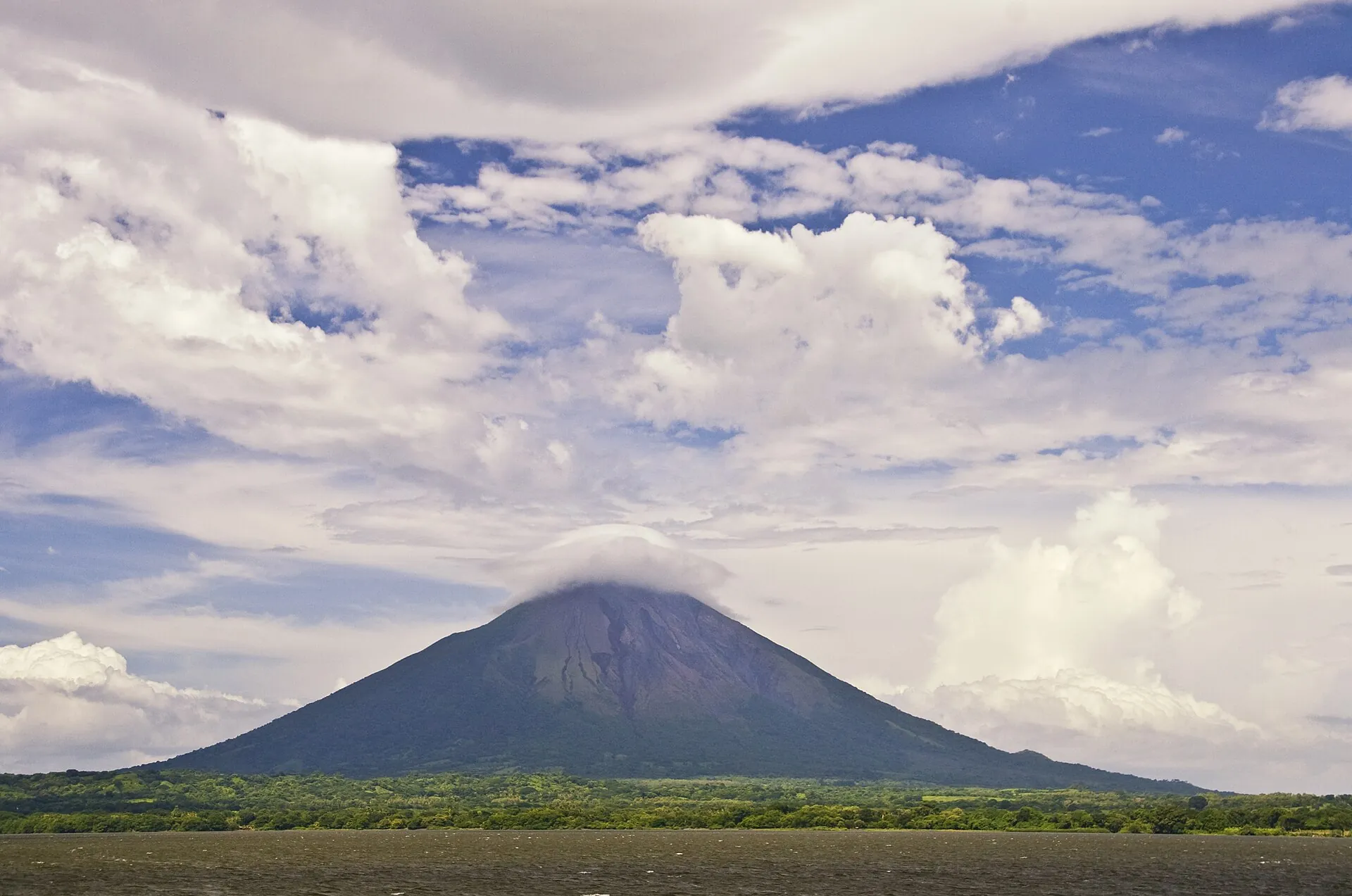 Der symmetrische Kegel des Concepción auf Ometepe mit einer Wolkenkappe über dem Gipfel, davor grüne Felder