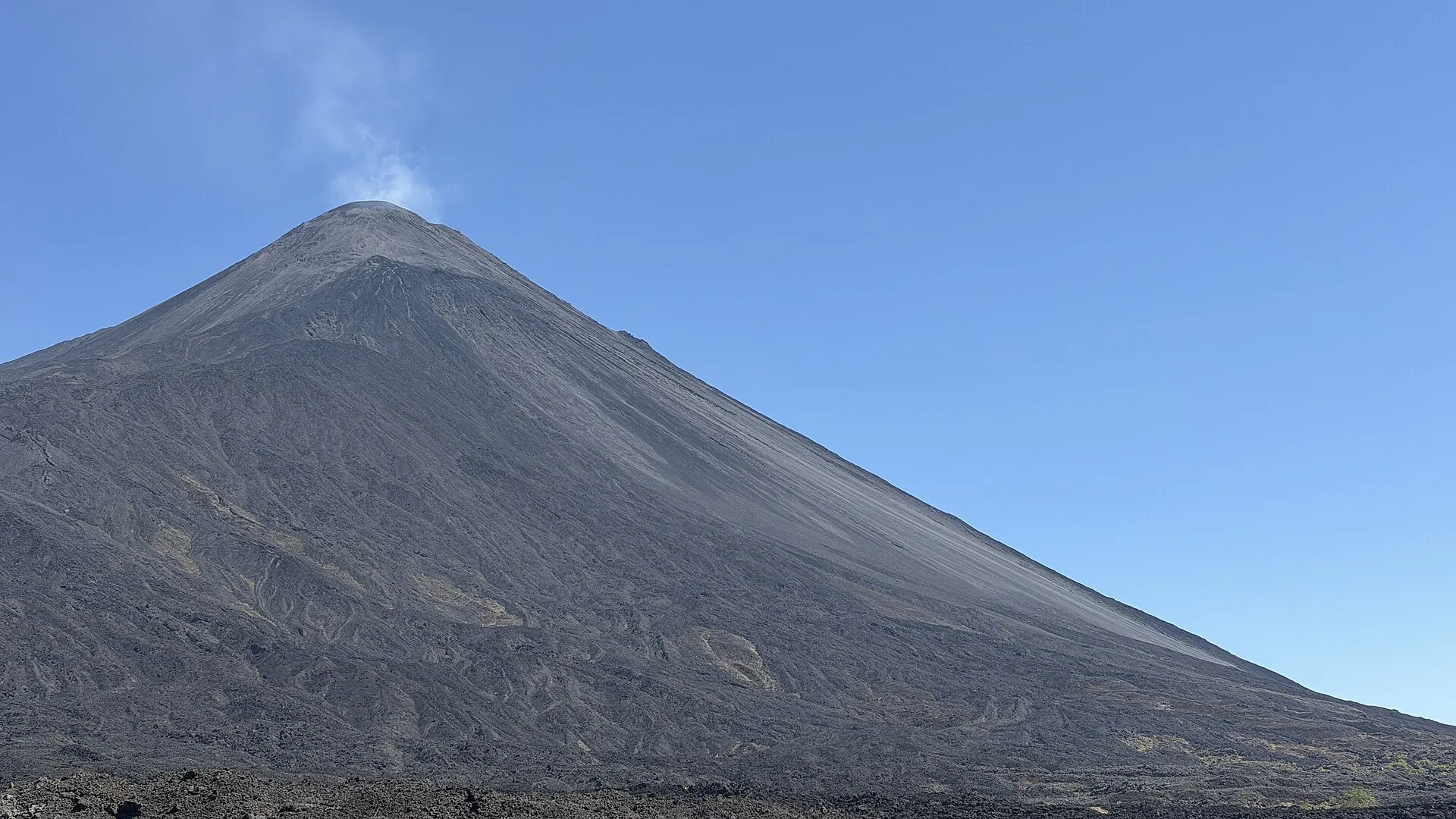 The gray ash cone of Pacaya against a blue sky, a thin white gas plume above the summit