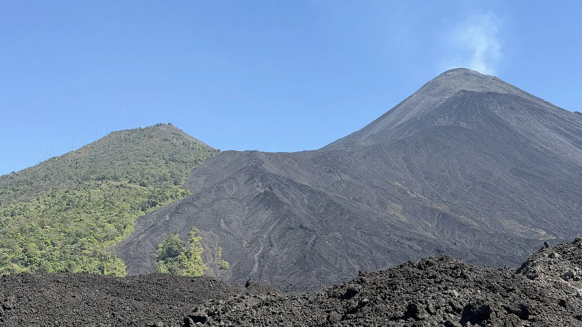 Black, jagged lava field at the foot of Pacaya, above it the gray cone with a thin gas plume at the crater
