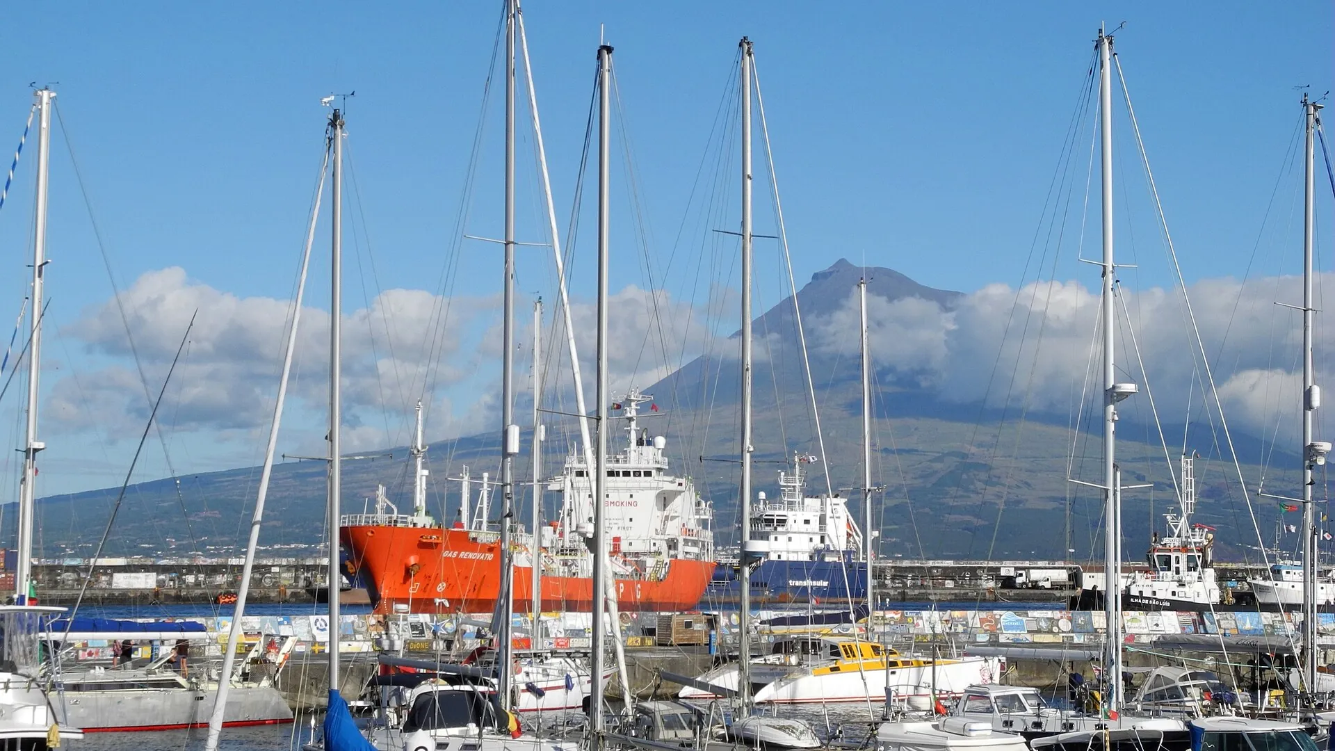 Der Yachthafen von Horta auf Faial mit Segelmasten, dahinter über dem Kanal der Kegel des Pico