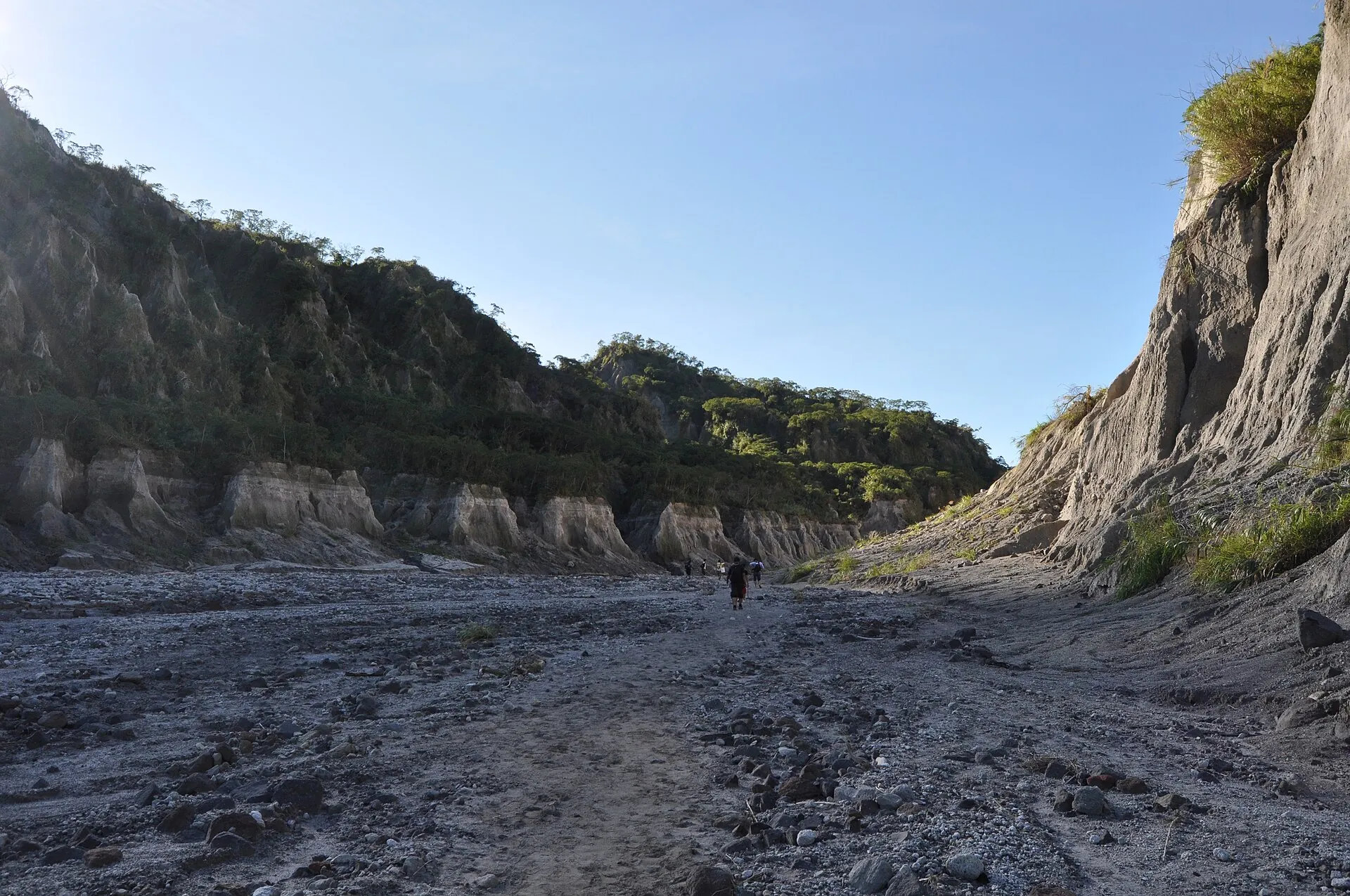 Zwei Wanderer im Flussbett des O'Donnell am Pinatubo, zwischen hohen hellgrauen Lahar-Wänden, blauer Himmel
