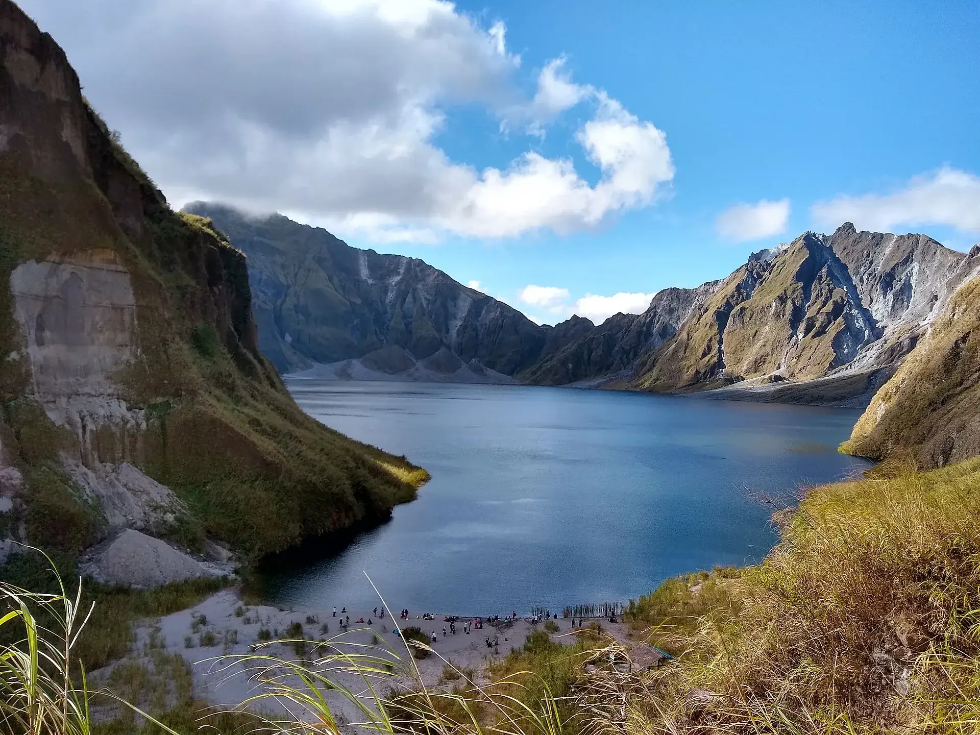 Der türkisblaue Kratersee des Pinatubo in der Caldera, steile Felswände ringsum, am Ufer eine Gruppe Besucher
