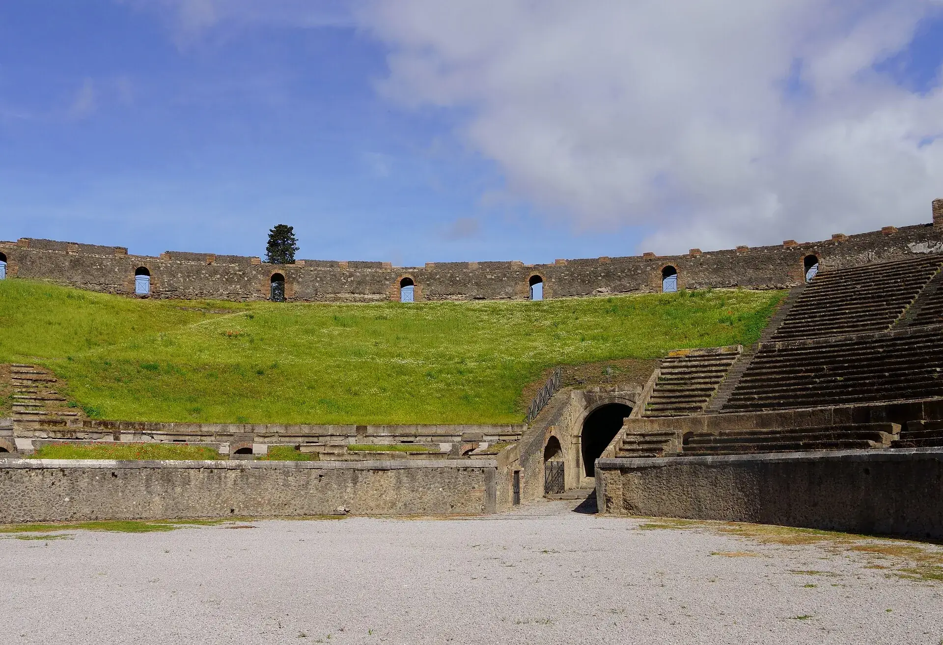 The amphitheater of Pompeii with its stone tiers under a blue sky, Vesuvius in the distance