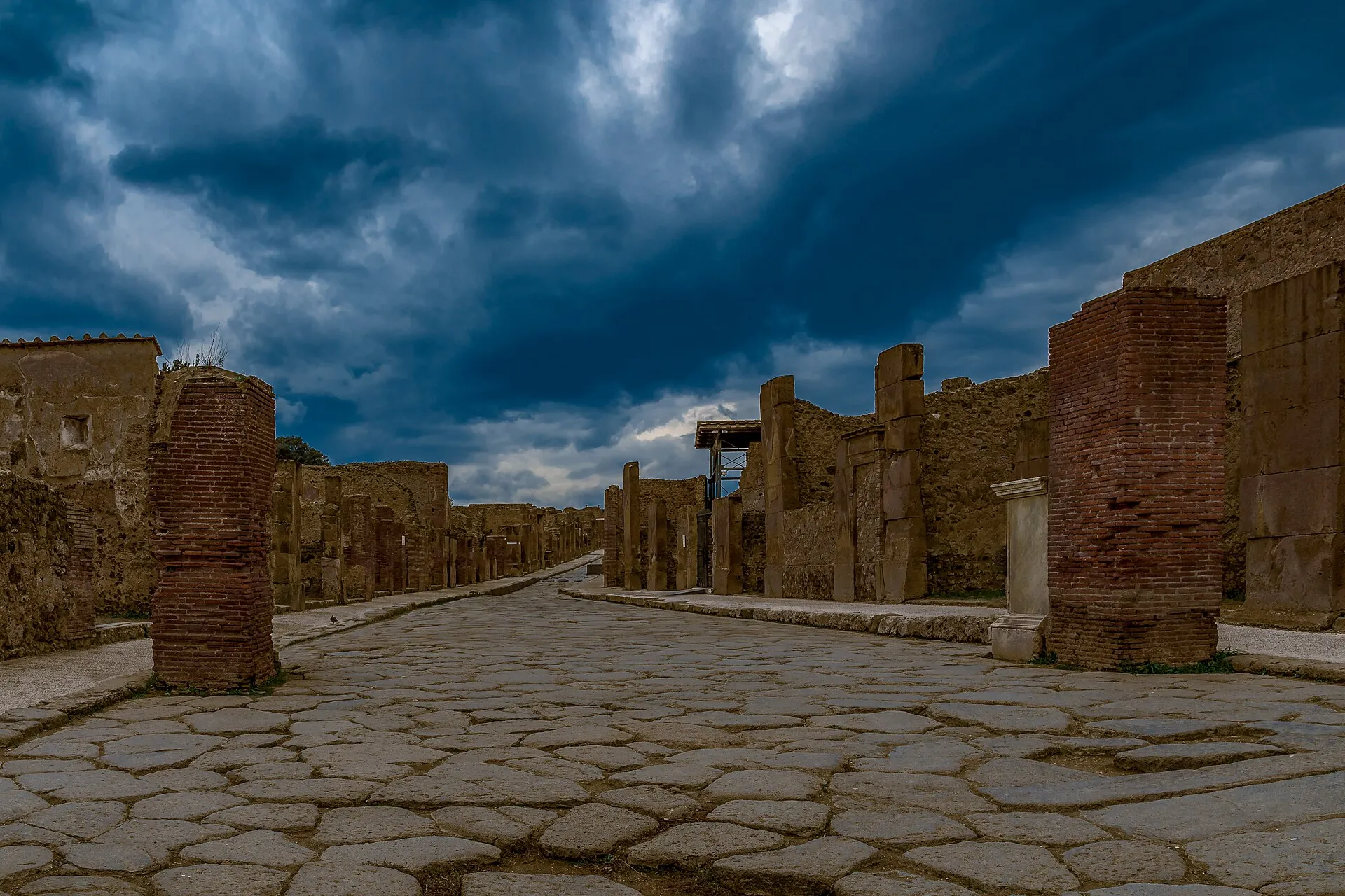 Via dell’Abbondanza in Pompeii: ancient large-block paving, house fronts, dark storm clouds