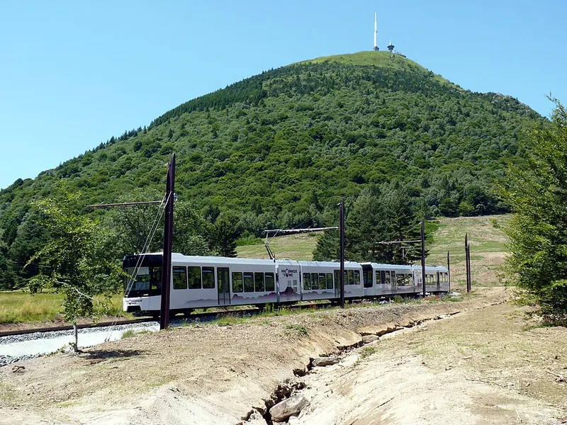 Die Zahnradbahn Panoramique des Dômes fährt auf der Flanke des Puy de Dôme bergauf, oben der Gipfel mit dem Sendemast