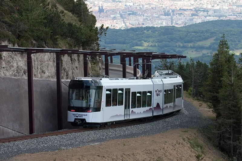 Ein Zug der Panoramique des Dômes fährt in die überdachte Bergstation auf dem Puy de Dôme ein, im Hintergrund die Ebene