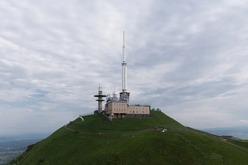 Der Gipfel des Puy de Dôme mit Sendemast, Wetterstation und Wiesen unter Wolken
