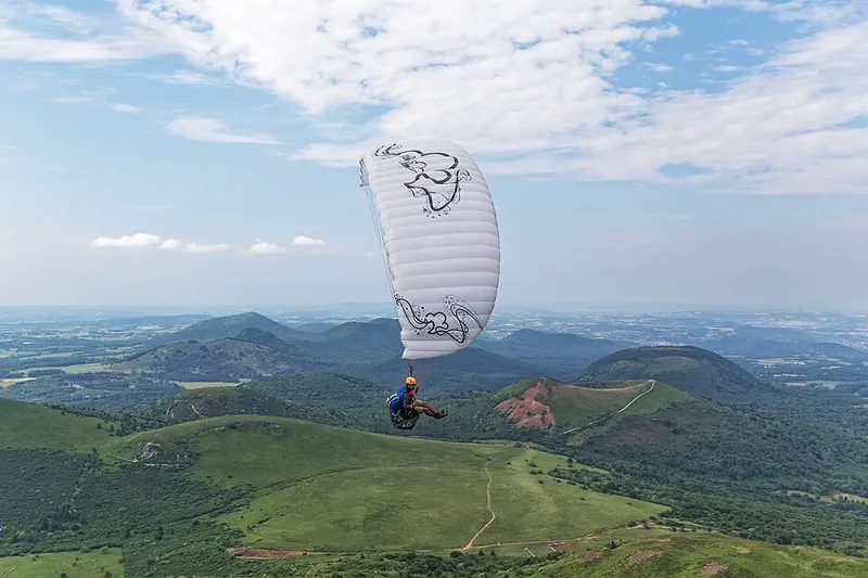 Ein Gleitschirm über den grünen Hängen des Puy de Dôme, darunter die Kegel der Chaîne des Puys