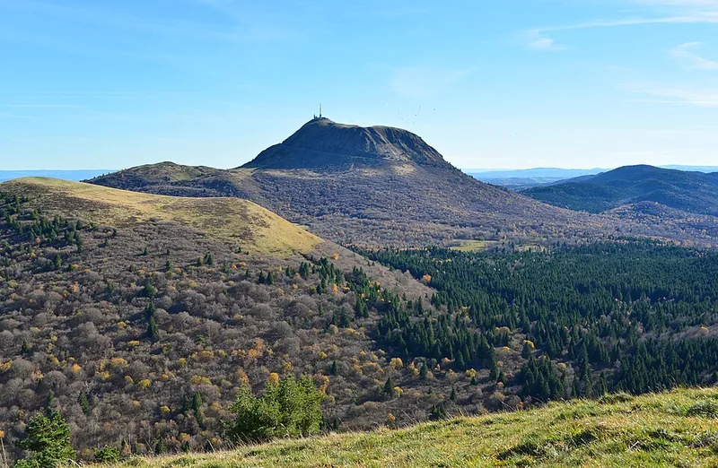 Der Puy de Dôme im Herbst: der runde Lavadom mit dem Sendemast über bewaldeten Kegeln der Chaîne des Puys