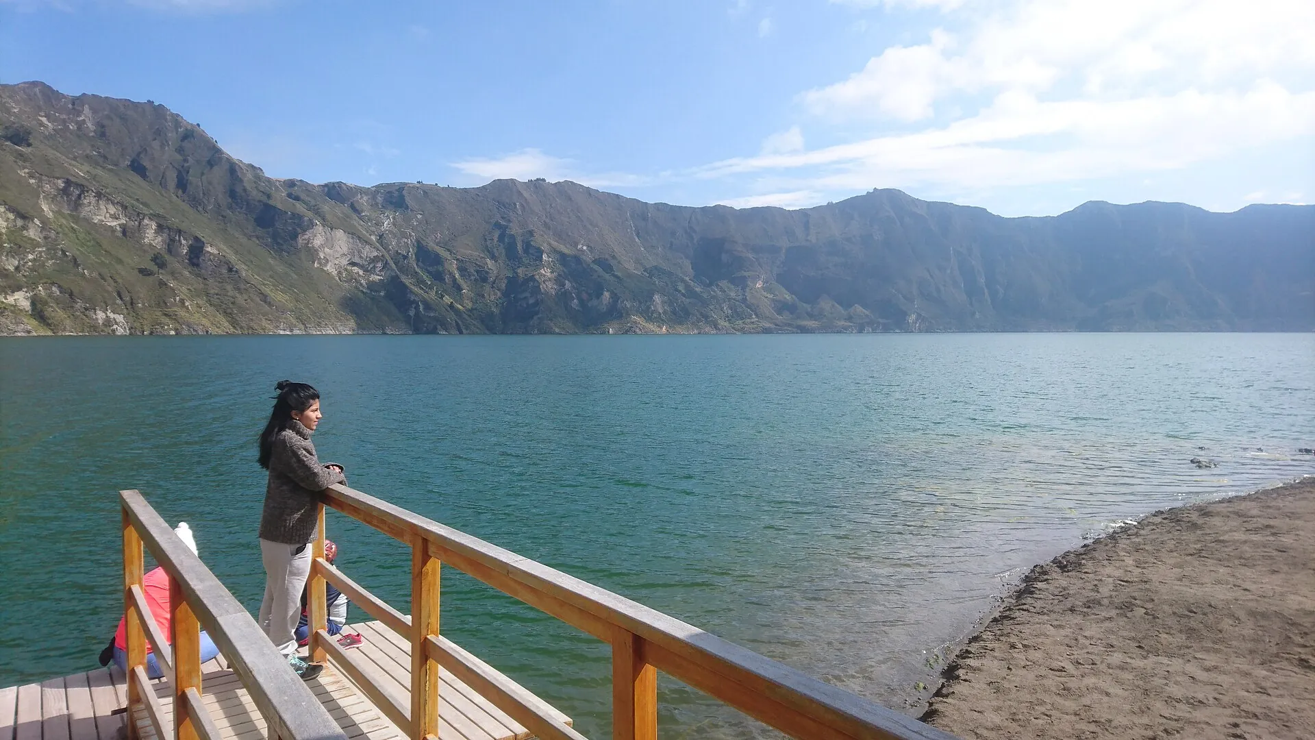 The wooden dock on the shore of Laguna Quilotoa, turquoise water, the crater wall behind