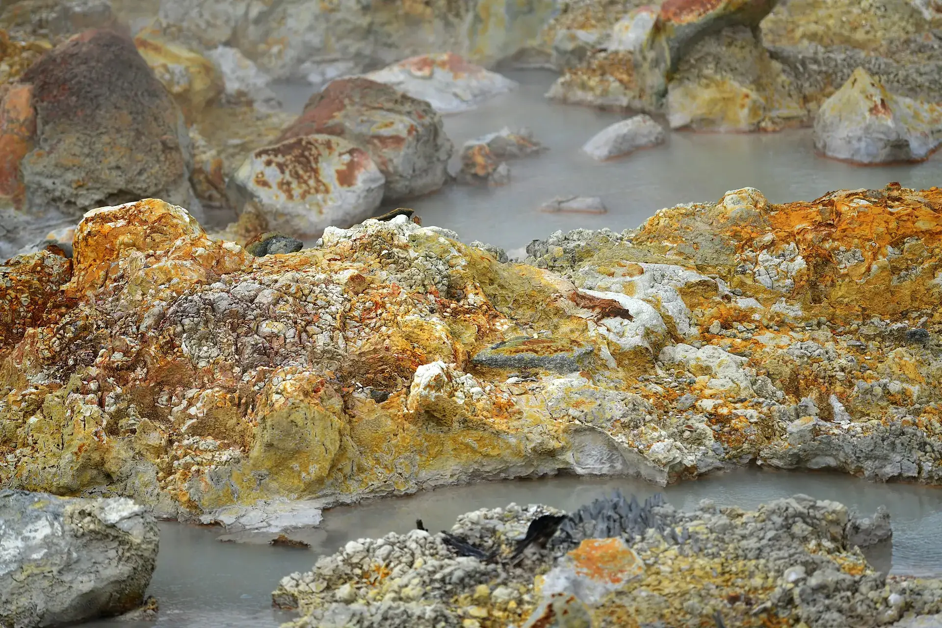 Yellow, orange and white encrusted rocks in a hot, gray pool in Rincón de la Vieja National Park