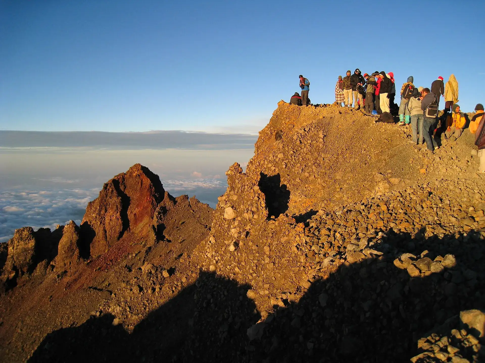 Hikers standing on the summit ridge of Mount Rinjani at sunrise, a sea of cloud below them