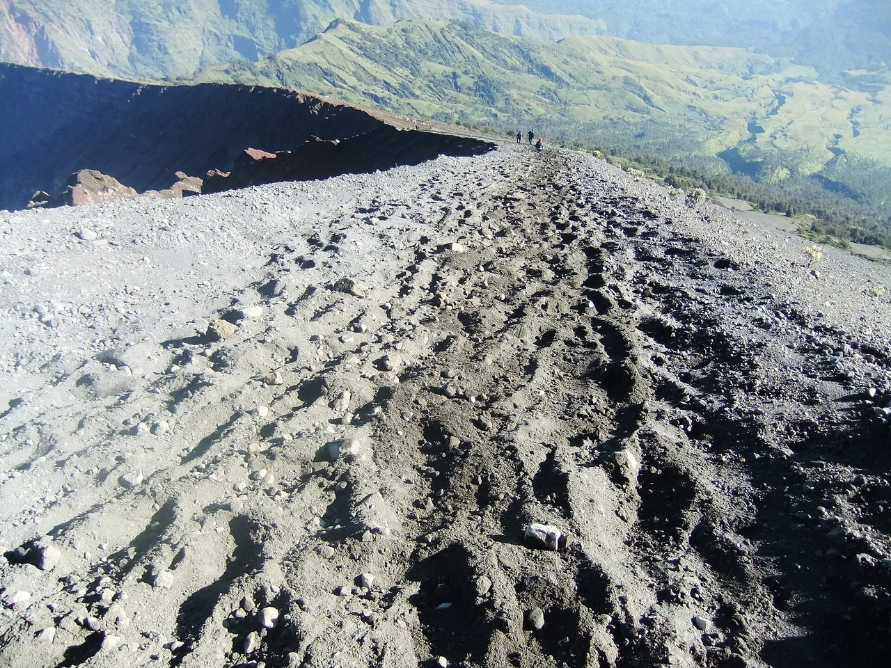 The summit ridge of Mount Rinjani by day: a broad back of loose gray volcanic sand and scree, the flank falling away on one side into the caldera