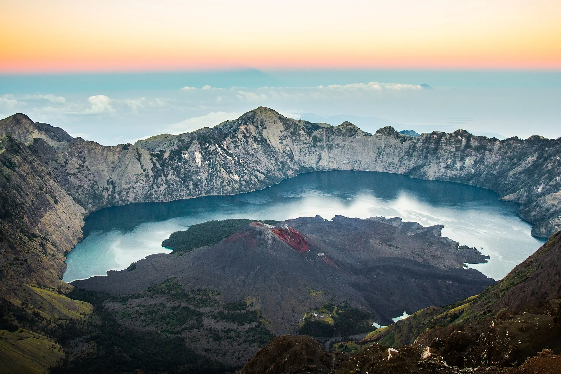 View across the caldera of Mount Rinjani on Lombok: the crater lake Segara Anak with the dark Barujari cone and its reddish crater, steep caldera walls all around