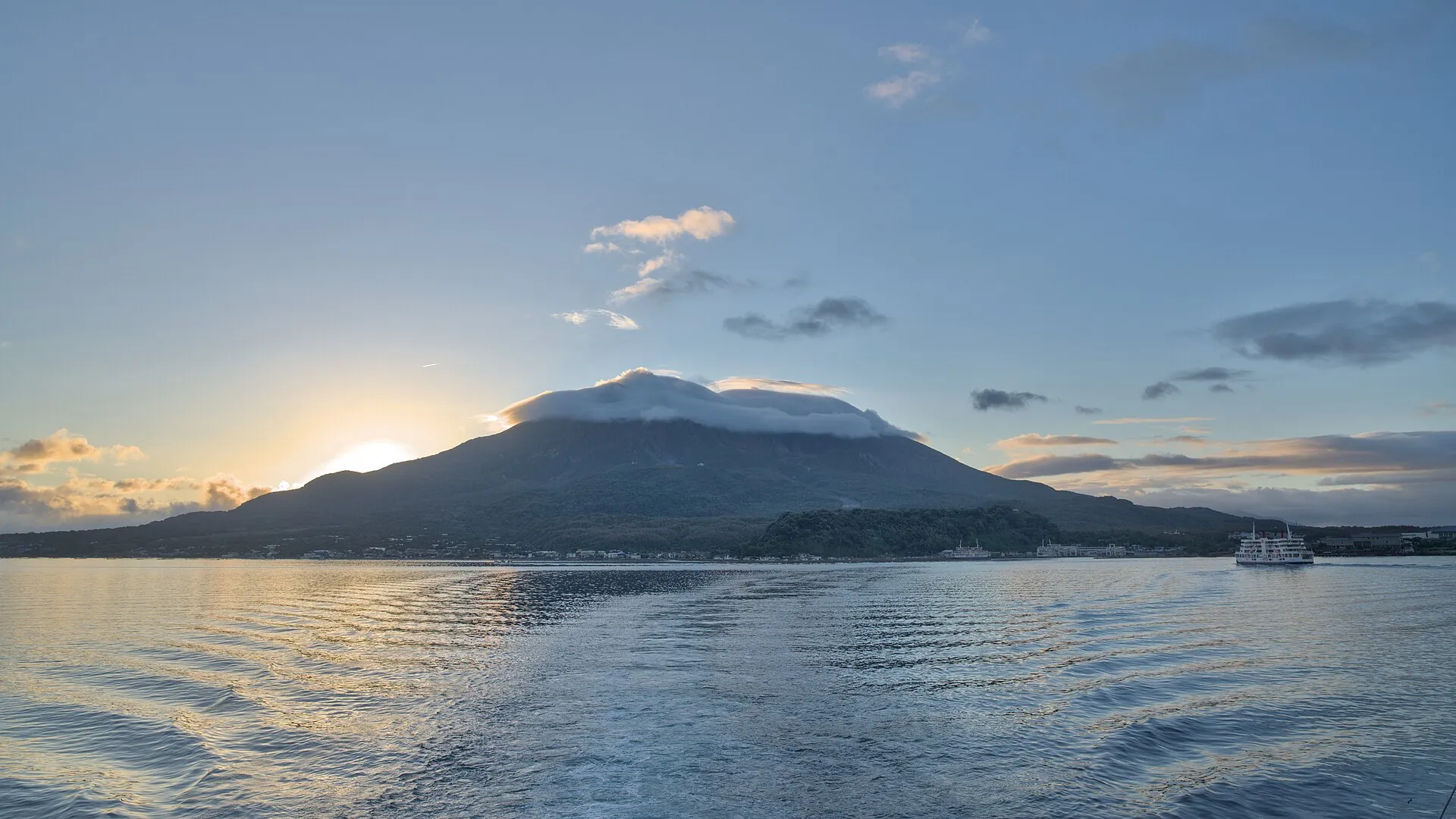 The volcano Sakurajima as a dark silhouette across Kinko Bay in the morning light, a ship on the water to the right
