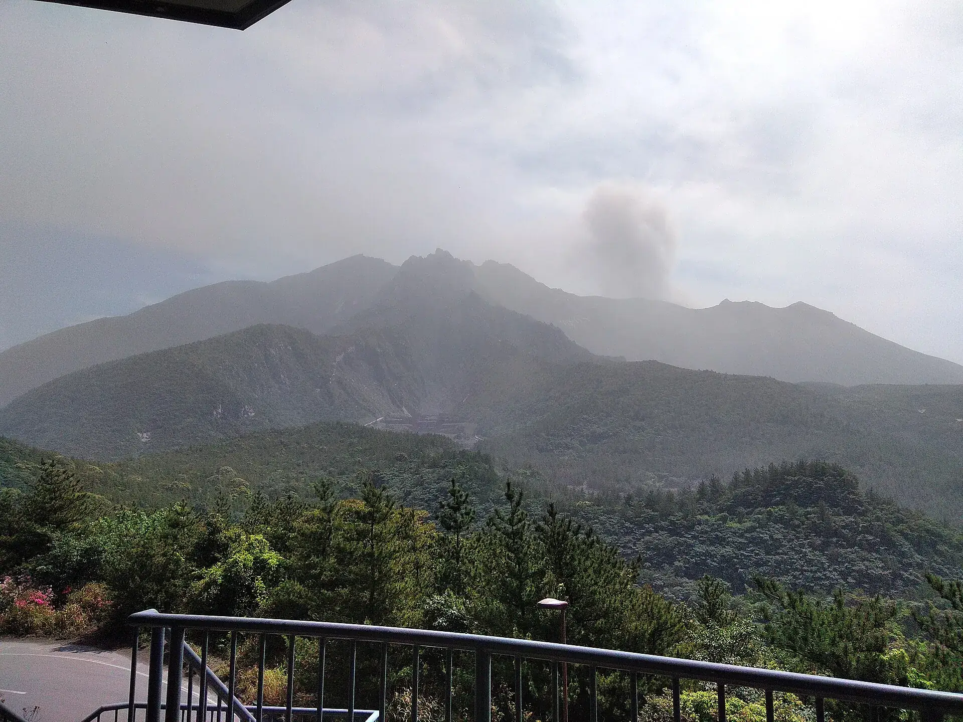 View from the railing of the Yunohira observatory toward the peaks of Sakurajima, with a dark ash cloud rising from them