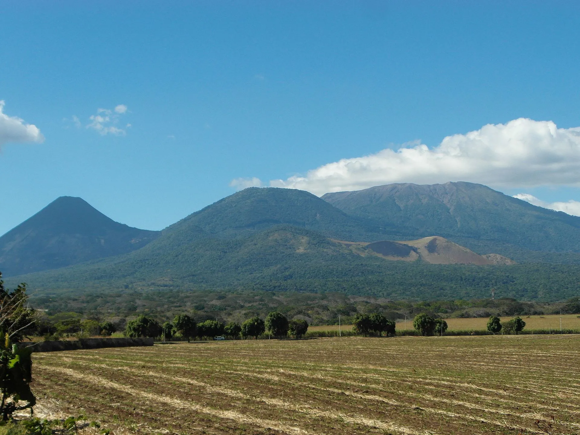 The three volcanoes of the Los Volcanes complex seen from the plain: Izalco, Cerro Verde and Santa Ana above a plowed field in El Salvador