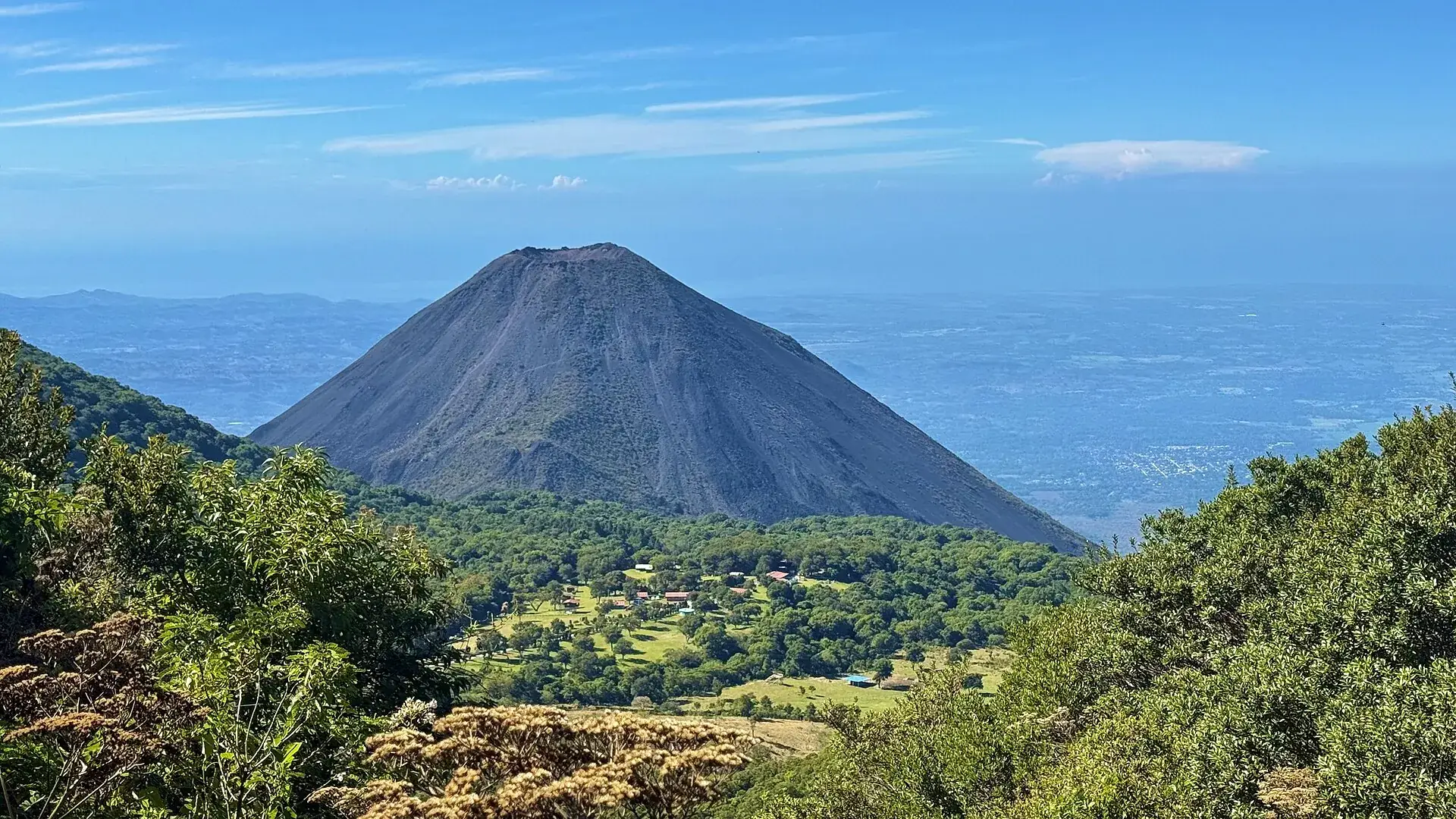 The dark, almost bare cone of Izalco seen from Santa Ana Volcano, green slopes and villages below