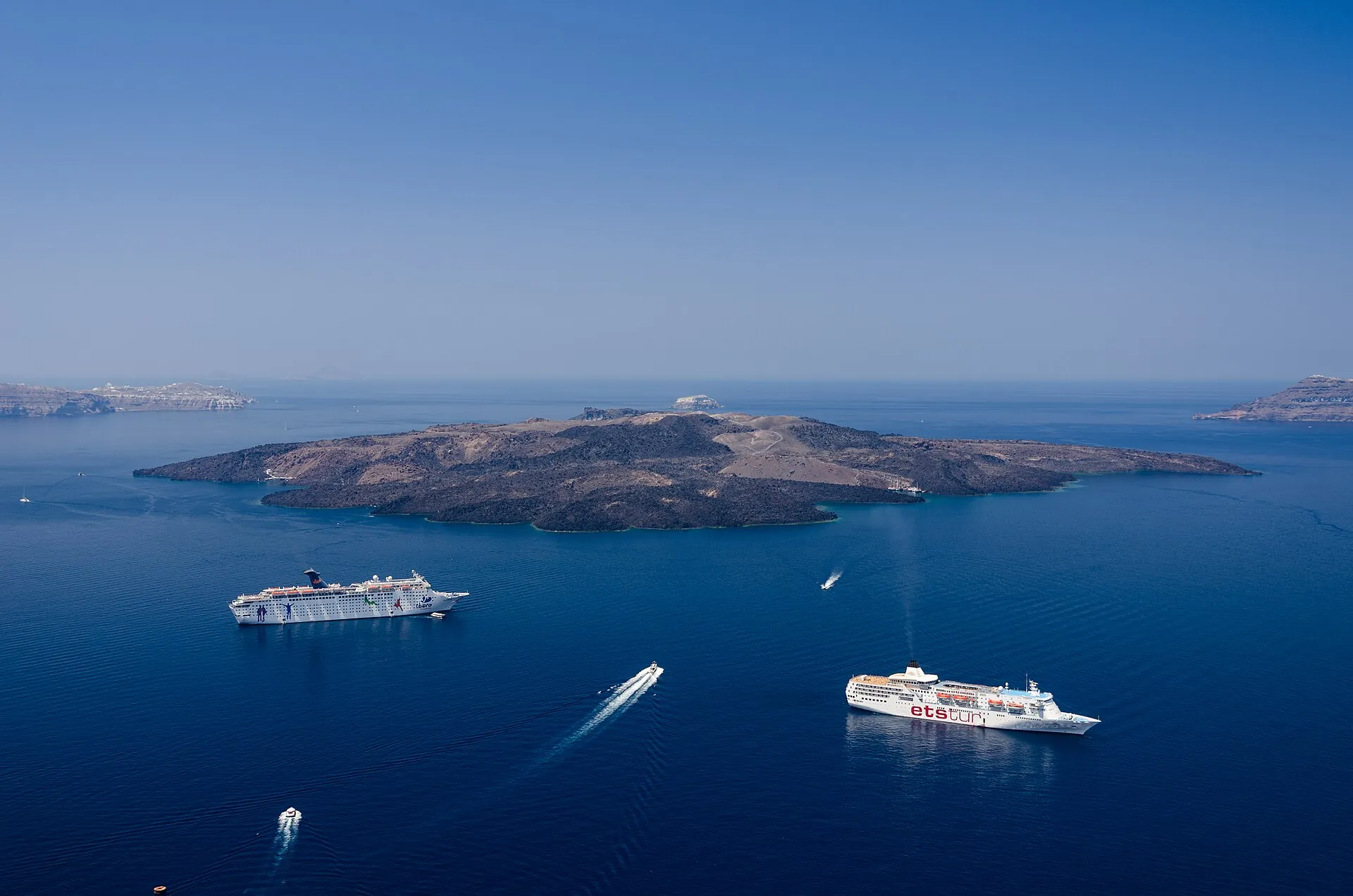 Blick von Fira über die Caldera von Santorin auf die dunkle Lavainsel Nea Kameni, davor Kreuzfahrtschiffe