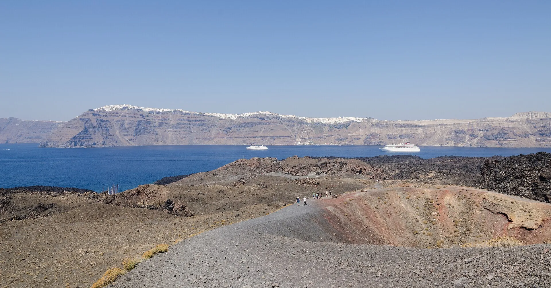 The gravel path over the crater rim of Nea Kameni, dark scoria underfoot, the pale caldera wall with the villages on the edge behind