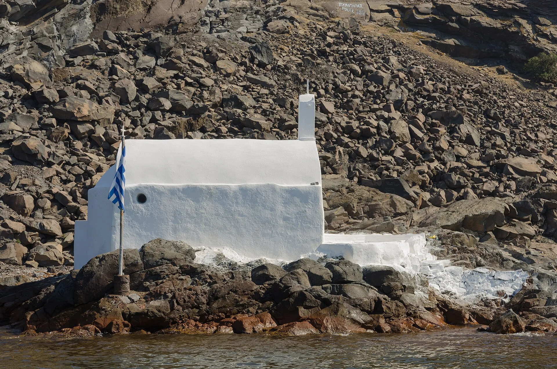 The small white chapel of Agios Nikolaos on the dark lava rocks of Palea Kameni, right by the water
