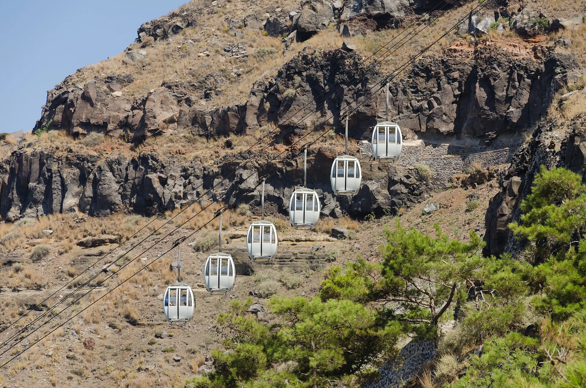 Cable-car gondolas between the old port and Fira hang above the steep caldera slope with pines