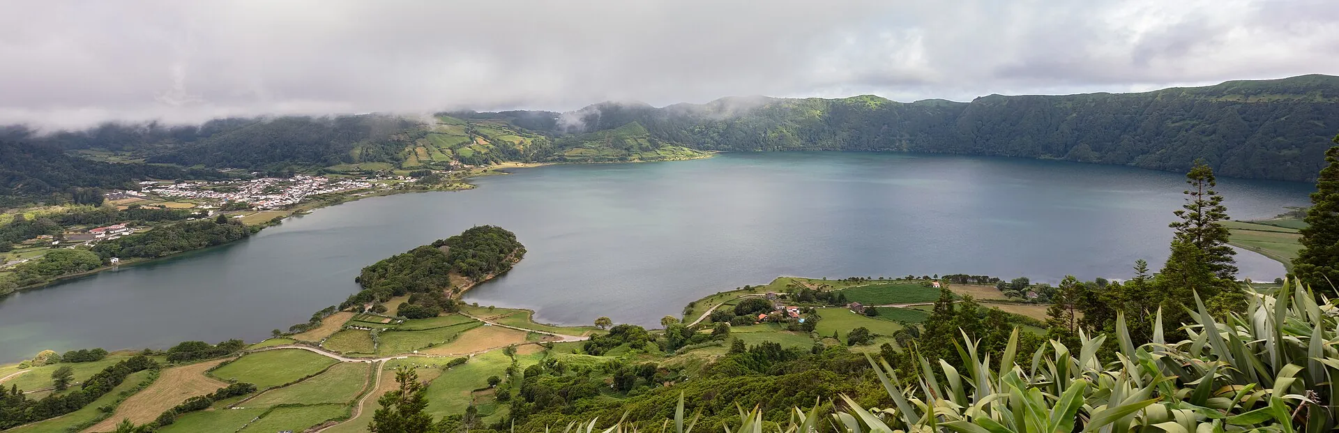 Die Lagoa Azul in Sete Cidades von oben: das Dorf mit weißen Häusern am Ufer, dahinter die grünen Kraterwände