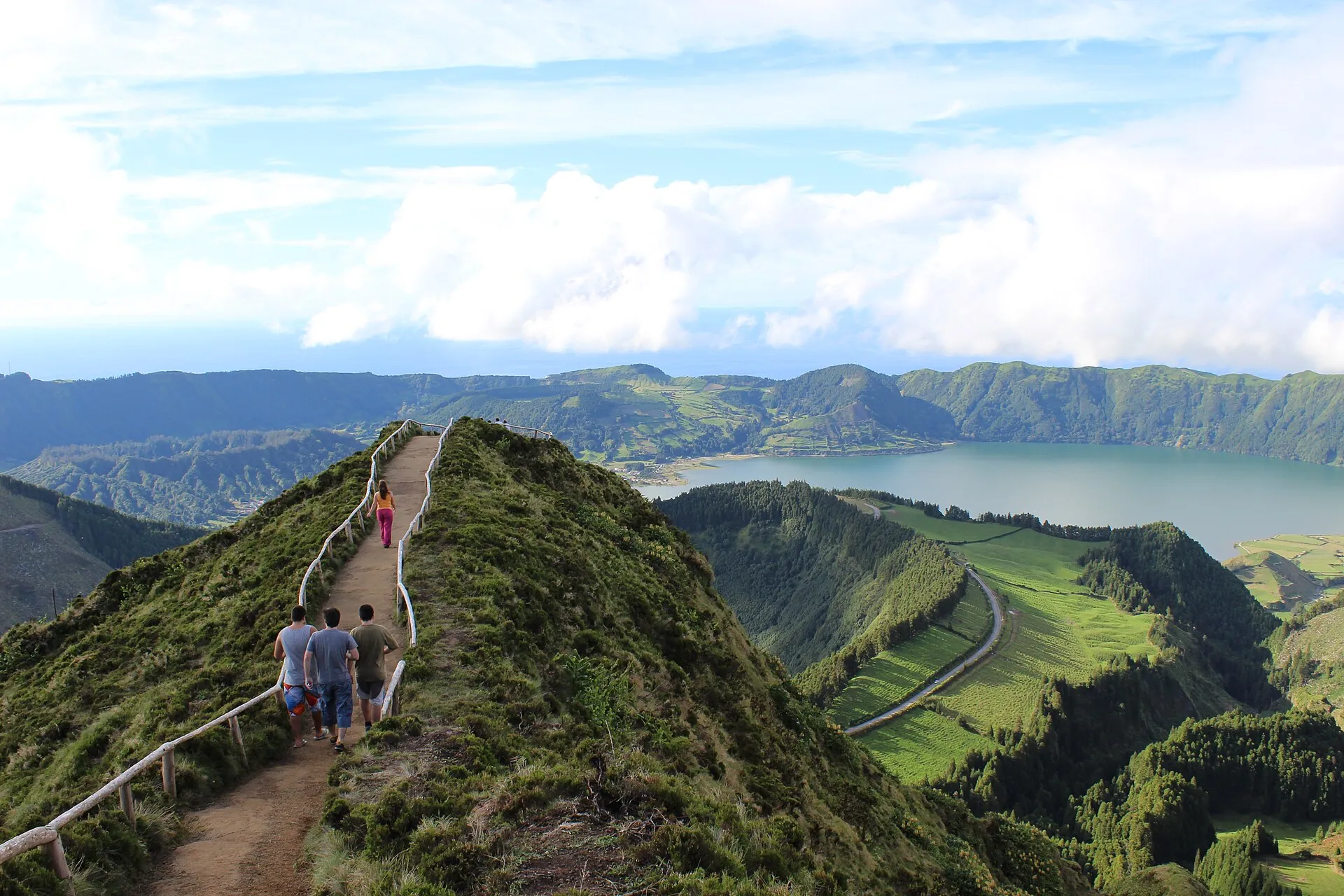 Hikers on the narrow crater-rim path to Boca do Inferno, the green slope falling away to the lakes on both sides