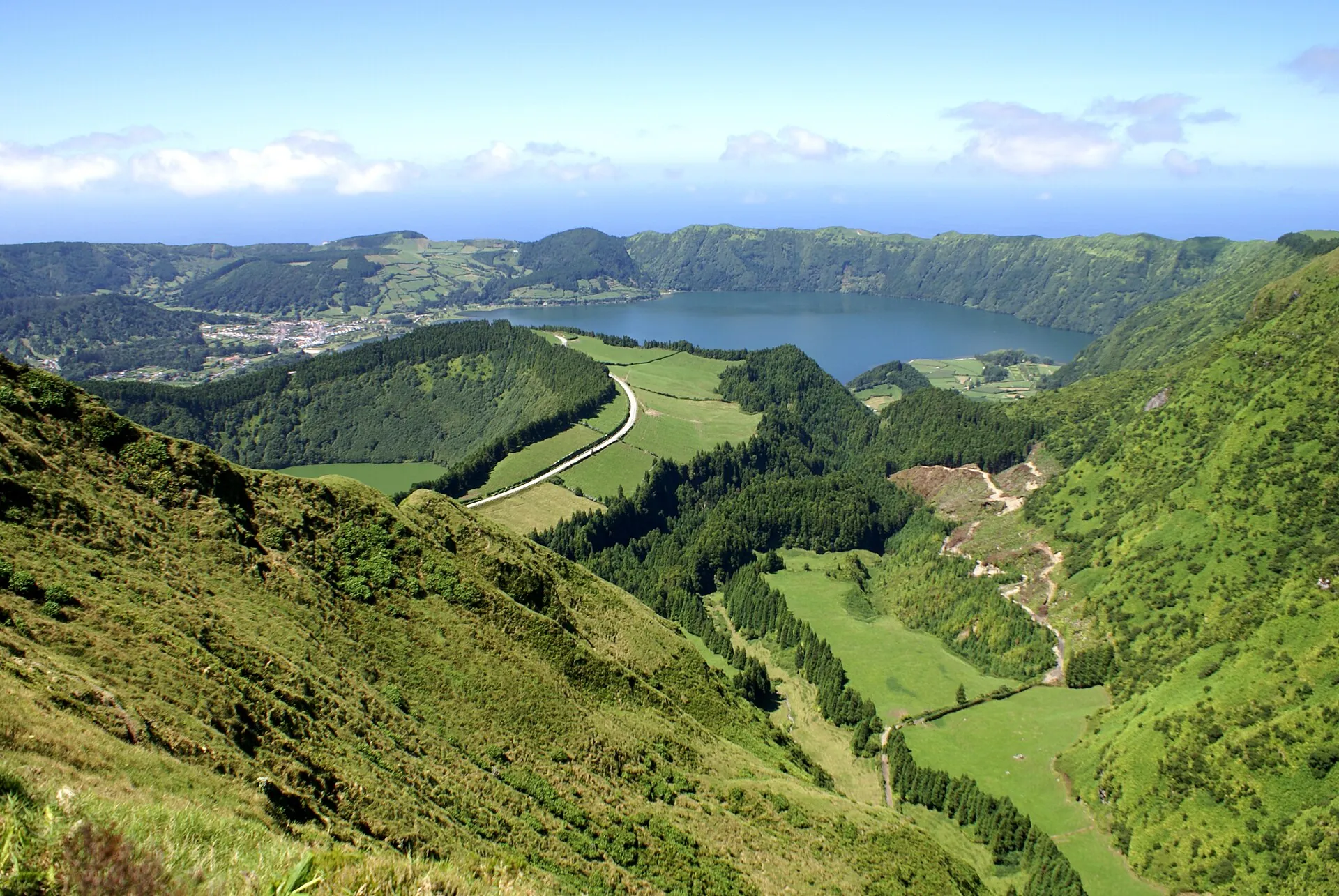 Blick von oben auf das Dorf Sete Cidades am Ufer der Lagoa Azul, die Straße zieht sich am Kraterrand entlang