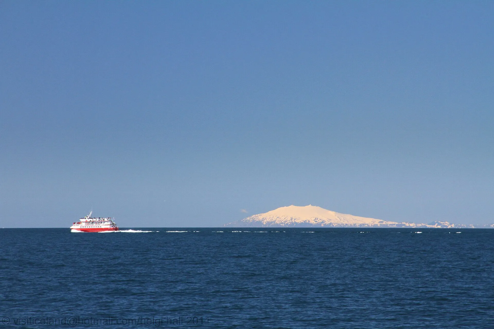 Der Snæfellsjökull als weißer Kegel jenseits der Faxaflói-Bucht, davor ein Ausflugsboot – der Blick von Reykjavík