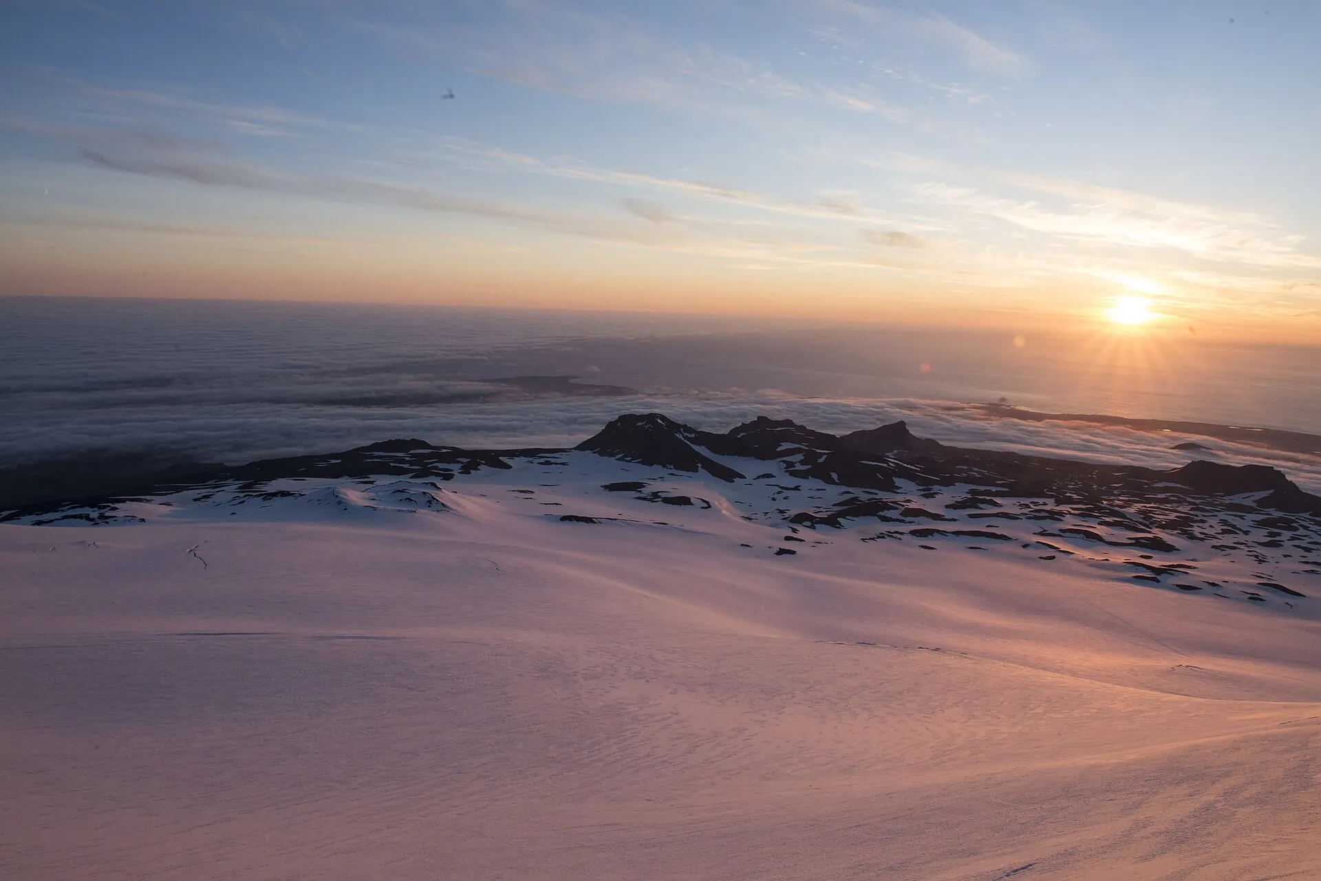 Blick vom Gipfel des Snæfellsjökull zur Mitternachtssonne am Sommersolstitium, rötliches Licht über dem Eis