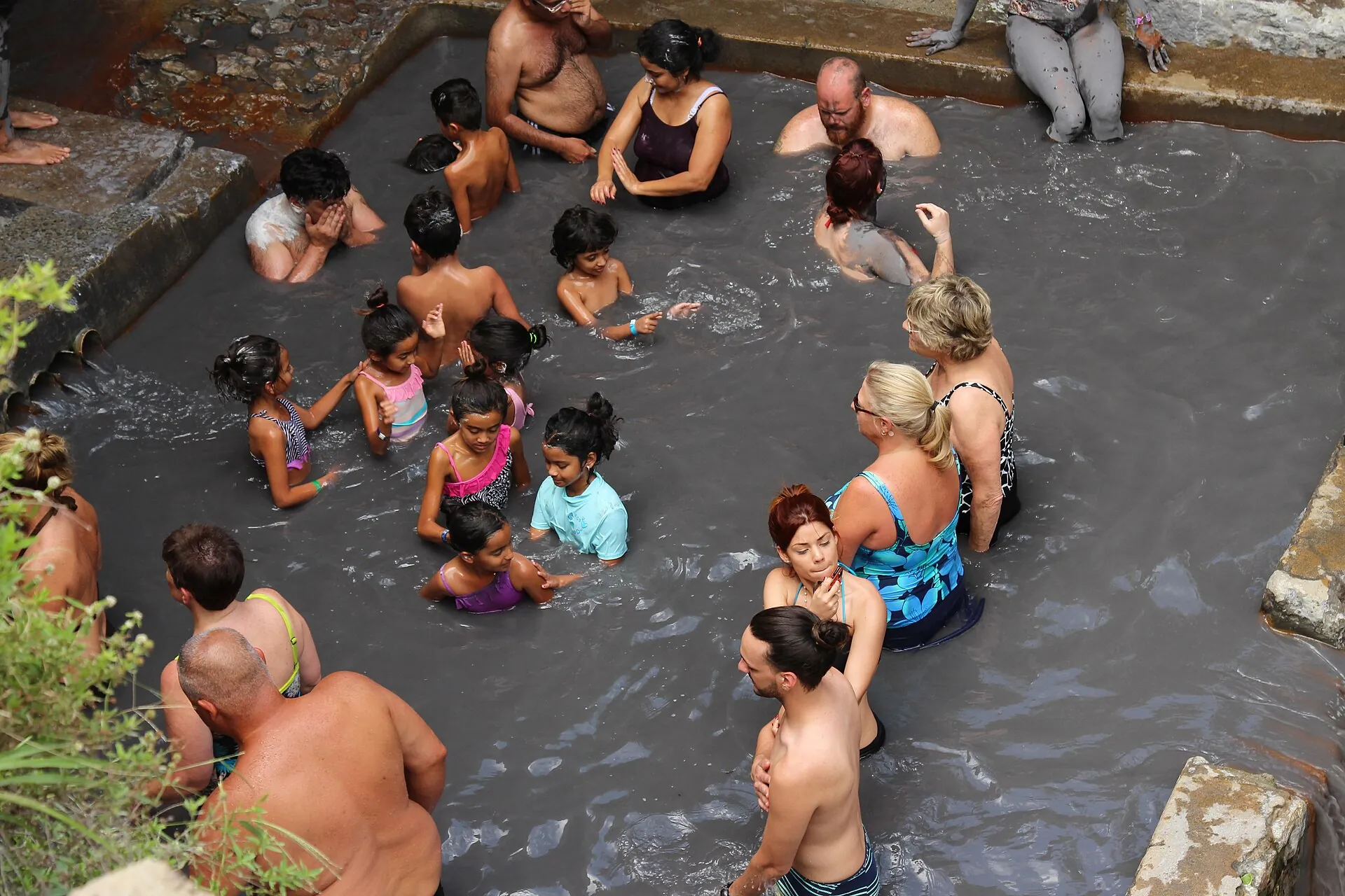 Besucher sitzen im grauen Schlammbecken der Sulphur Springs und reiben sich Vulkanschlamm auf die Haut