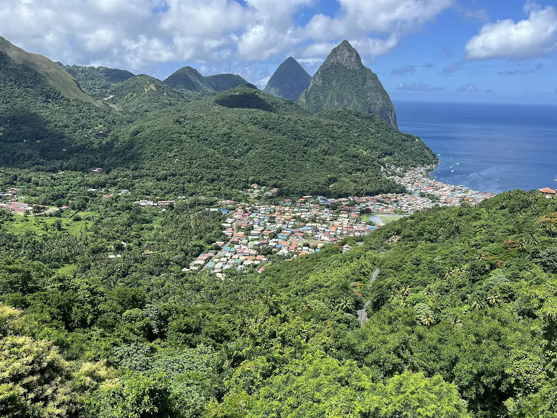 Die beiden Pitons auf St. Lucia über der Bucht von Soufrière, davor Palmen und die Küstenstraße