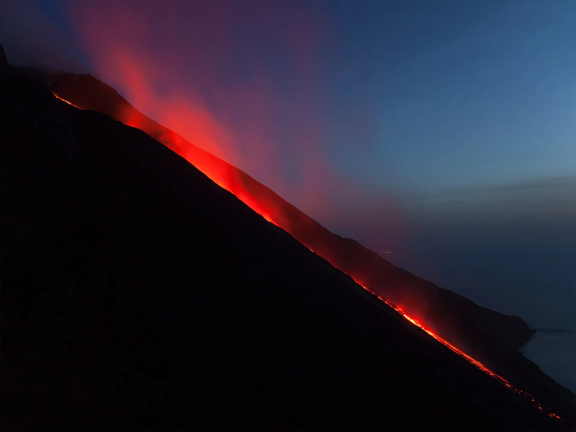 The Sciara del Fuoco on Stromboli at night: red-glowing lava trails run down the black flank to the sea