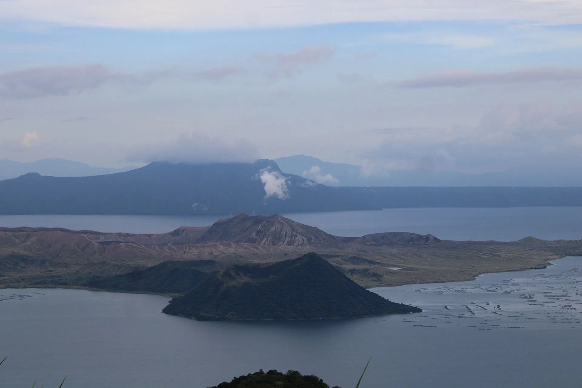 Weiße Dampffahne über dem Hauptkrater der Vulkaninsel im Taalsee, dahinter der Calderarand unter Wolken