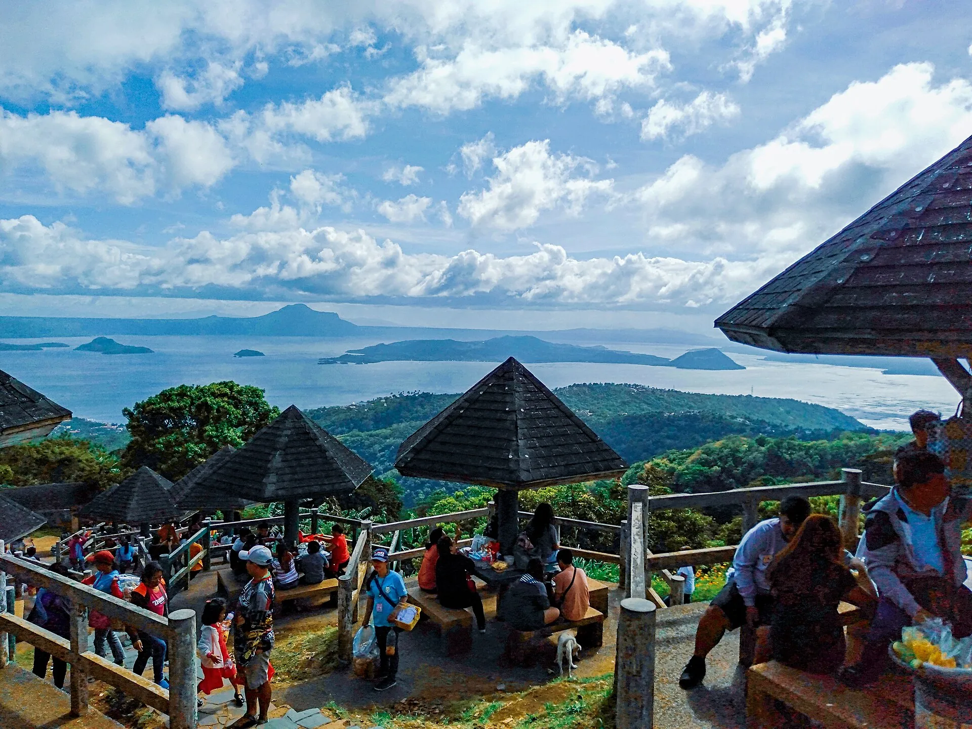 Aussichtsplattform im Picnic Grove in Tagaytay mit Besuchern unter Strohdächern, dahinter der Taalsee und die Vulkaninsel