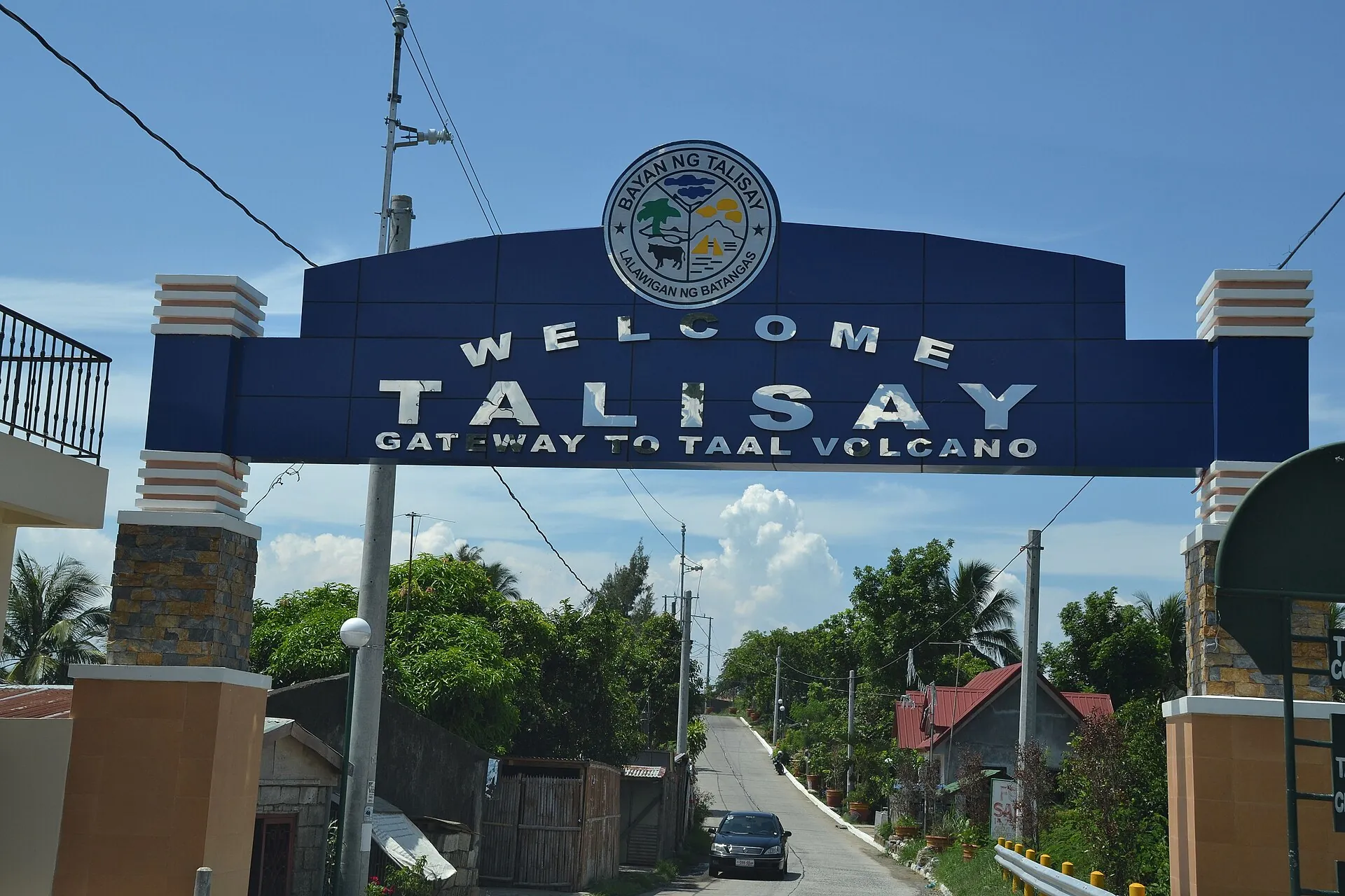 Blauer Torbogen mit der Aufschrift „Welcome Talisay – Gateway to Taal Volcano“ über der Straße ins Seeufer-Städtchen Talisay