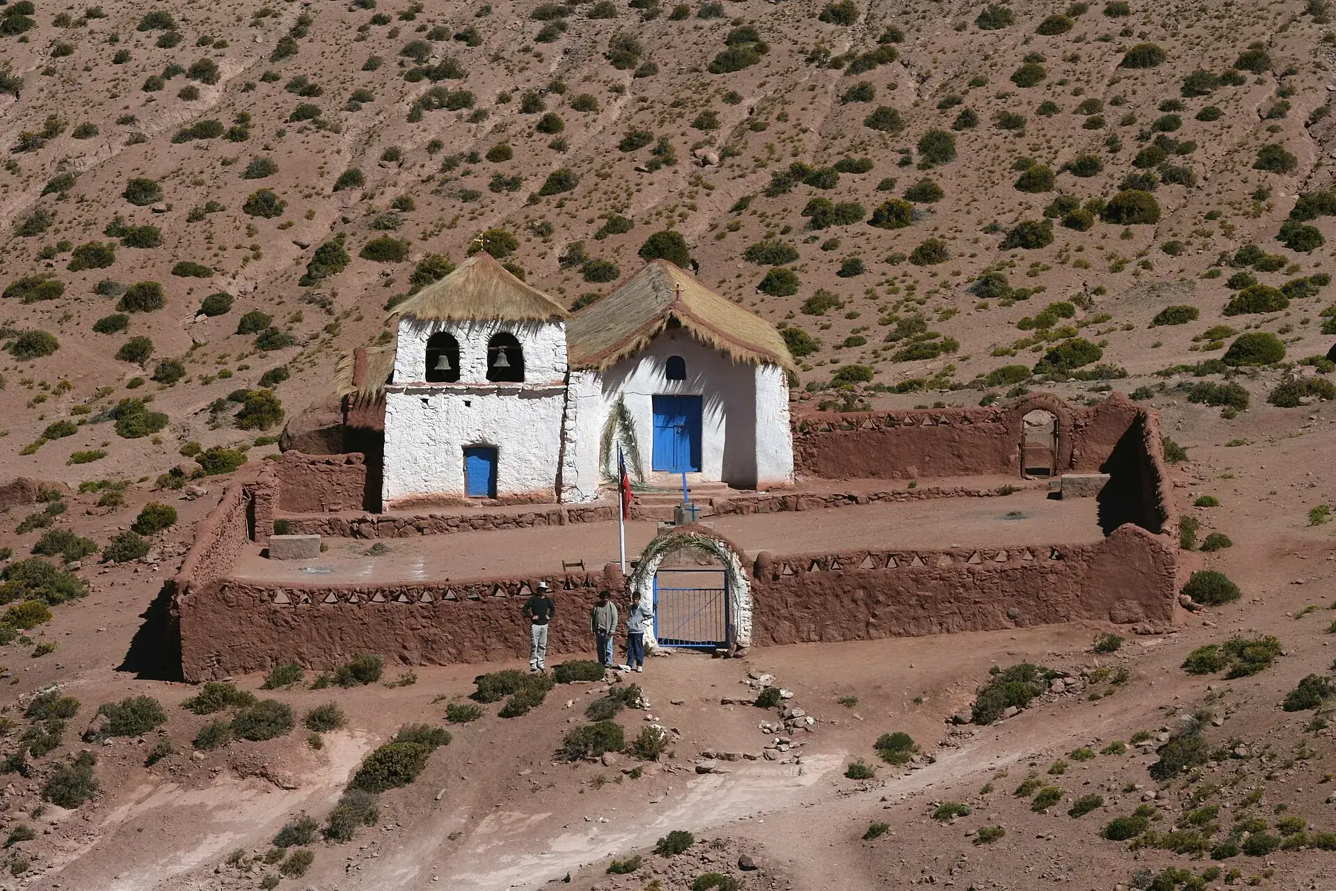 The white adobe church of Machuca with its thatched roof and stone wall at 4,000 m, brown hills behind