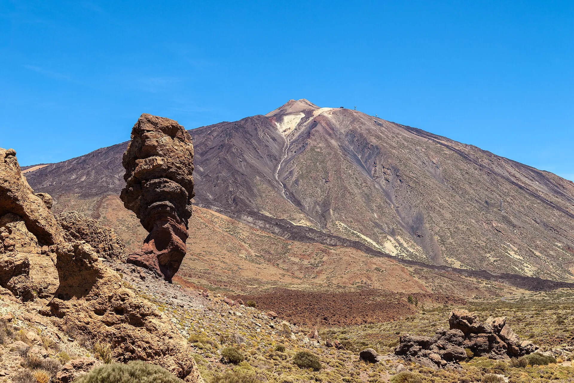 Roque Cinchado, a slender tower of red-brown rock, in front of the pale cone of Teide under a deep blue sky