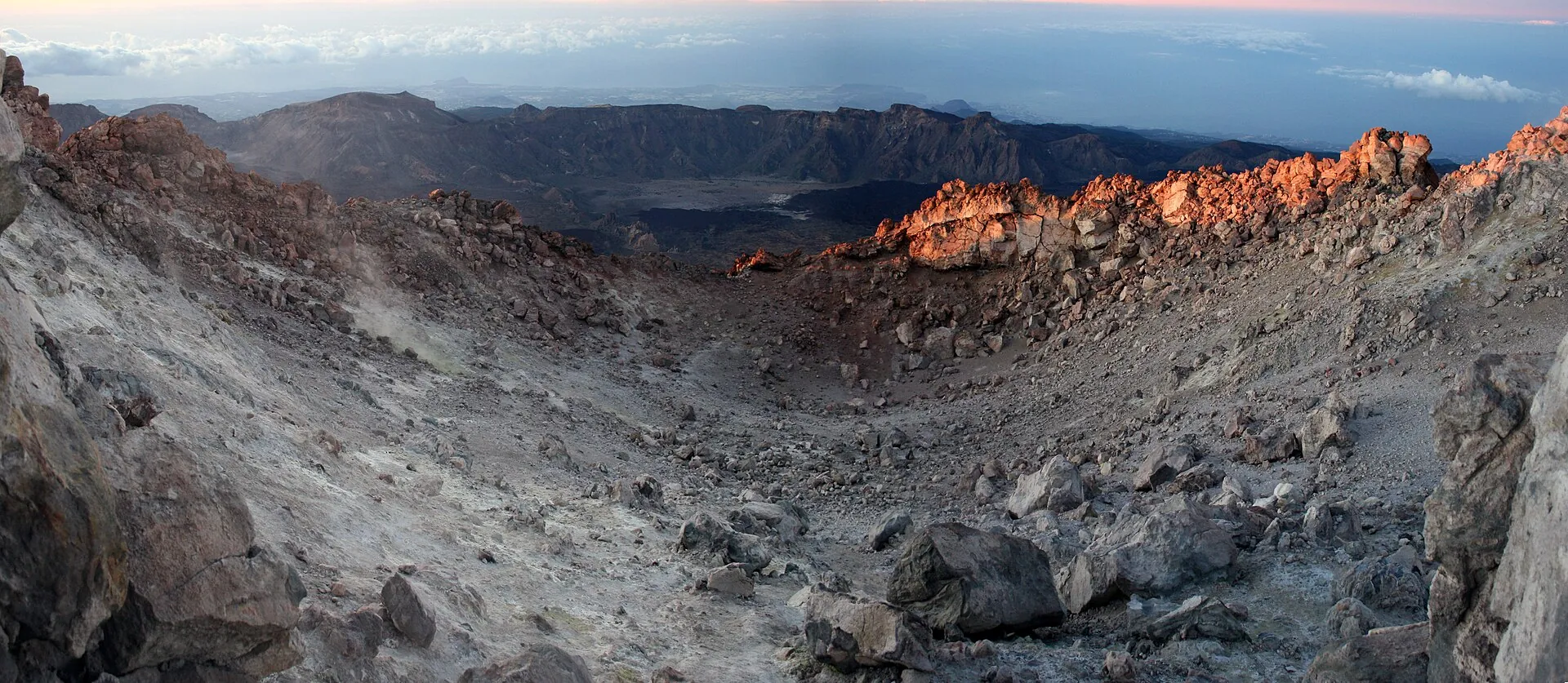 The summit crater of Teide: pale sulphur deposits and red-brown rock in the crater, the sea of clouds behind
